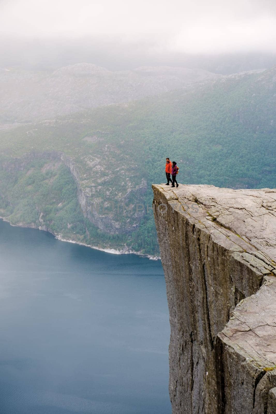 Preikestolen, Norway, Two people stand on the edge of a cliff overlooking a fjord in Norway. The cliff is known as Preikestolen, or Pulpit Rock, and is a popular tourist destination.