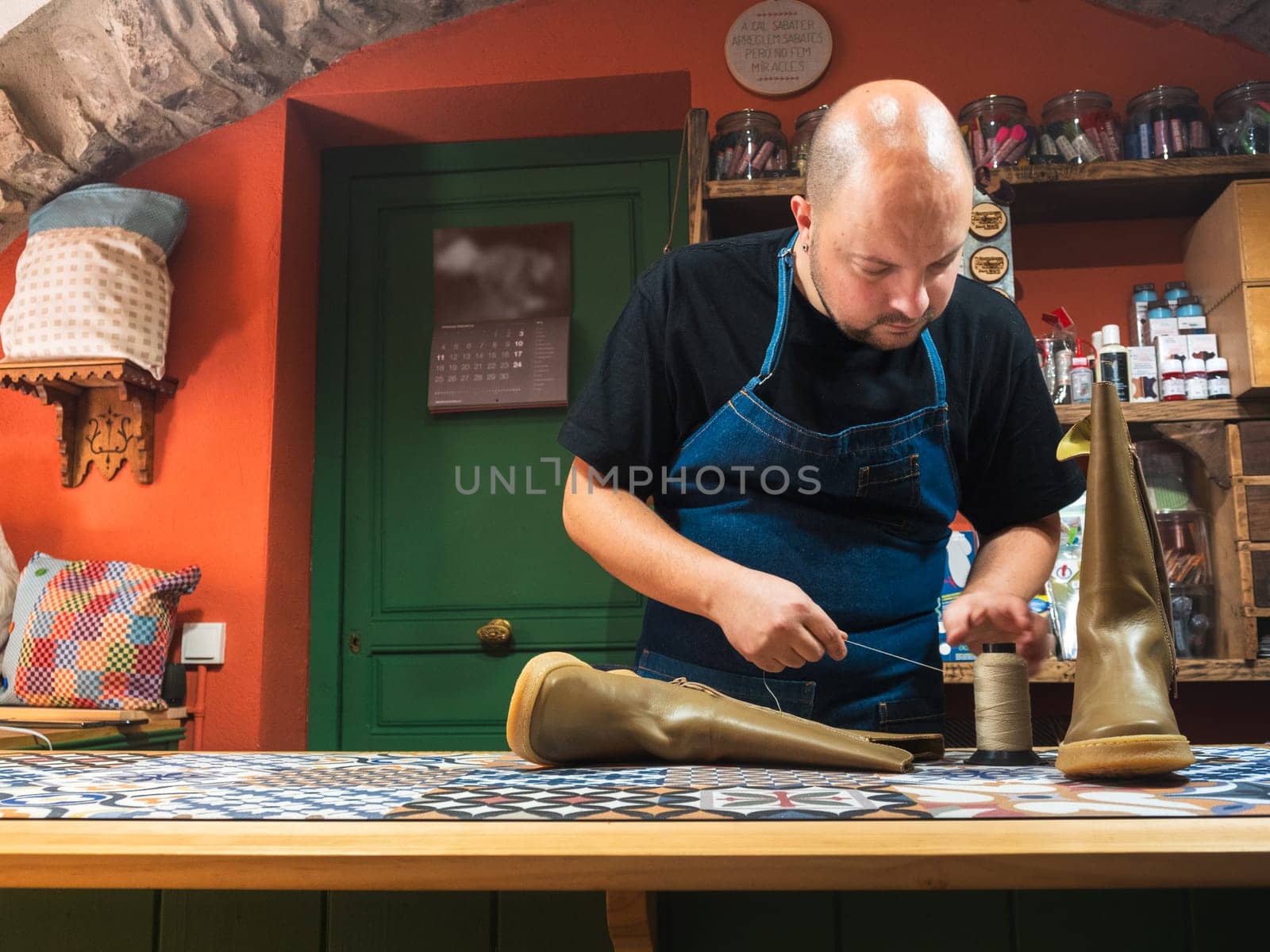Shoemaker at store counter picking up thread to repair boots. Trades and businesses. 