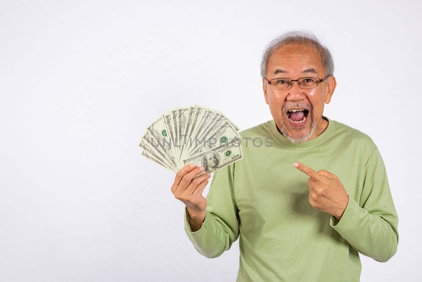 Portrait Asian smiling old man is holding a bunch of money banknotes and pointing studio shot isolated on white background. happy elderly positive excited hold dollar banknotes fan, Financial success