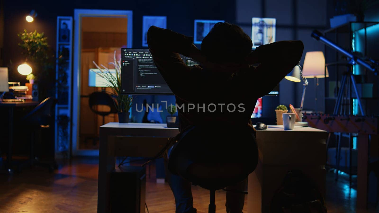 Man doing IT support job from home office, stretching after sitting on desk chair all day. Programmer loosening up, relaxing after typing on computer for long period of time, camera B