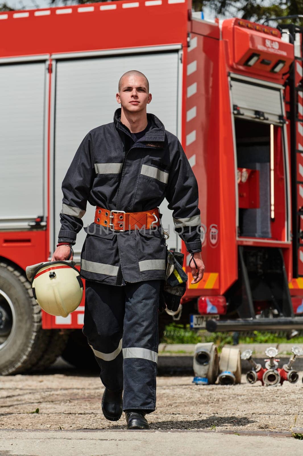 A firefighter, adorned in professional gear, stands confidently beside a fire truck following a grueling firefighting training session