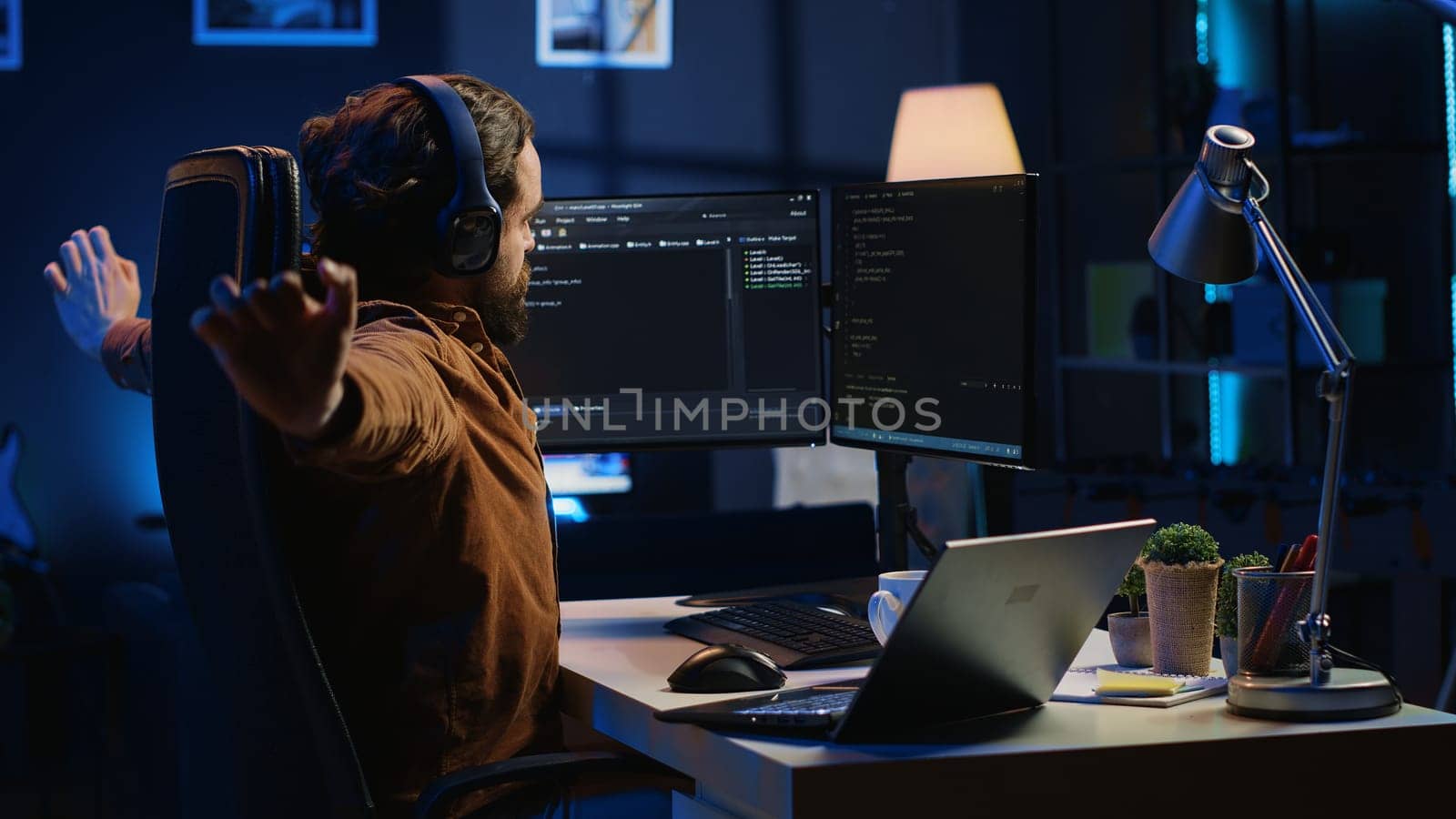 Software programmer taking break from coding, putting headphones on and stretching on desk chair during remote job shift. IT professional pausing tasks, listening music, loosening up, camera A