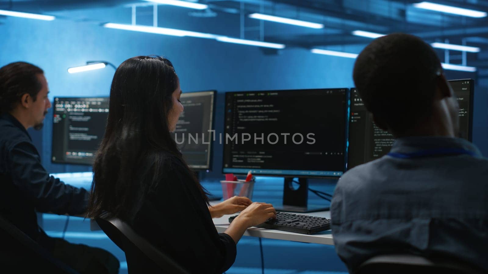 Multiethnic team of engineers working in high tech server hub, using PCs to analyze data. Multiracial group of employees examining infrastructure in data center, ensuring system integrity and security