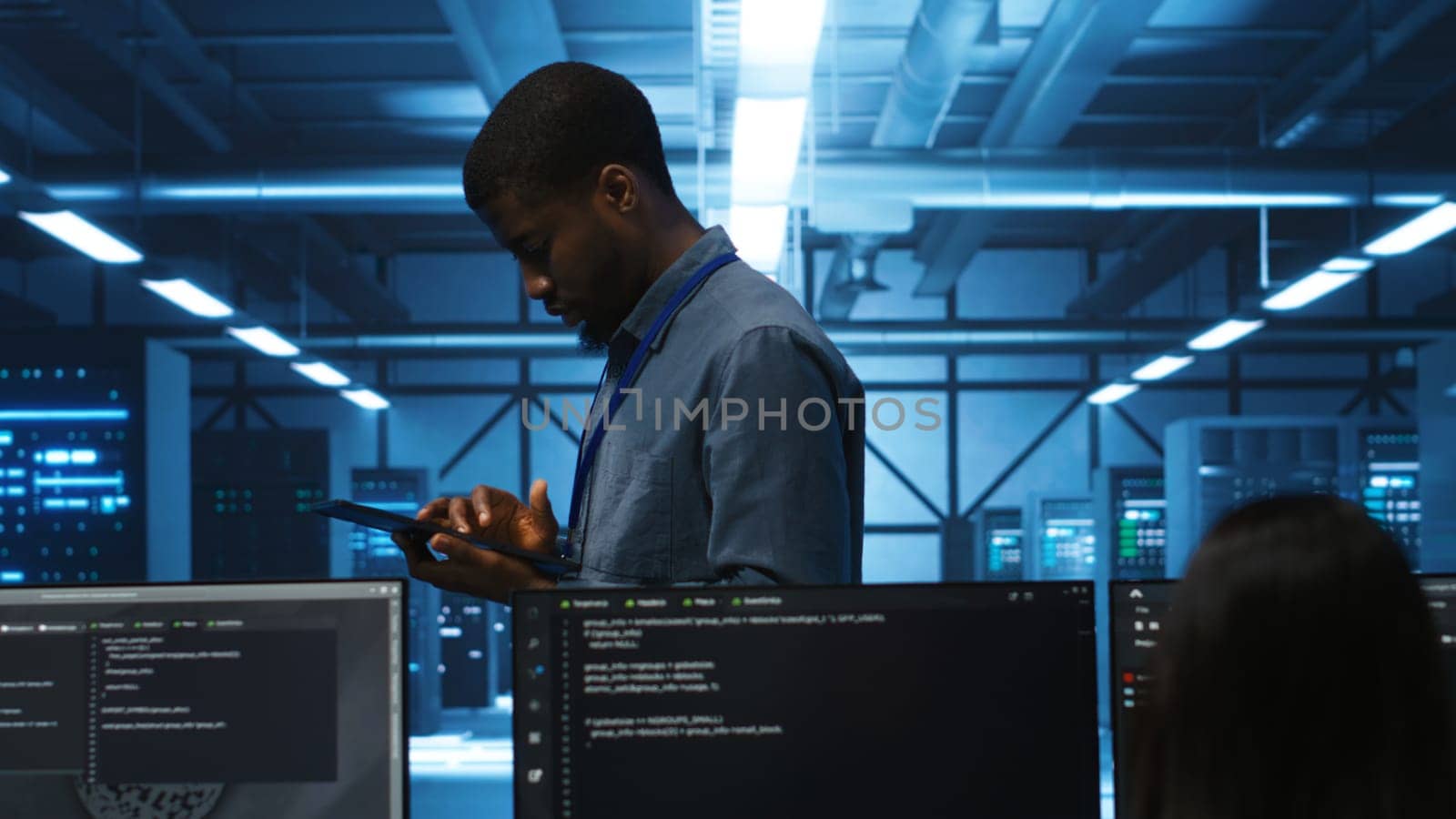 Technician doing system analysis using tablet, doing needed adjustments in supercomputers server farm. Engineer overseeing data center housing storage infrastructure supporting critical IT workloads