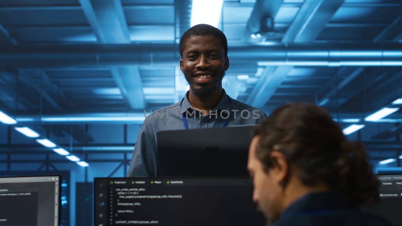 Portrait of cheerful african american manager supervising team in server room providing computing resources for workloads. Jolly supervisor oversees technicians in data center mending supercomputers