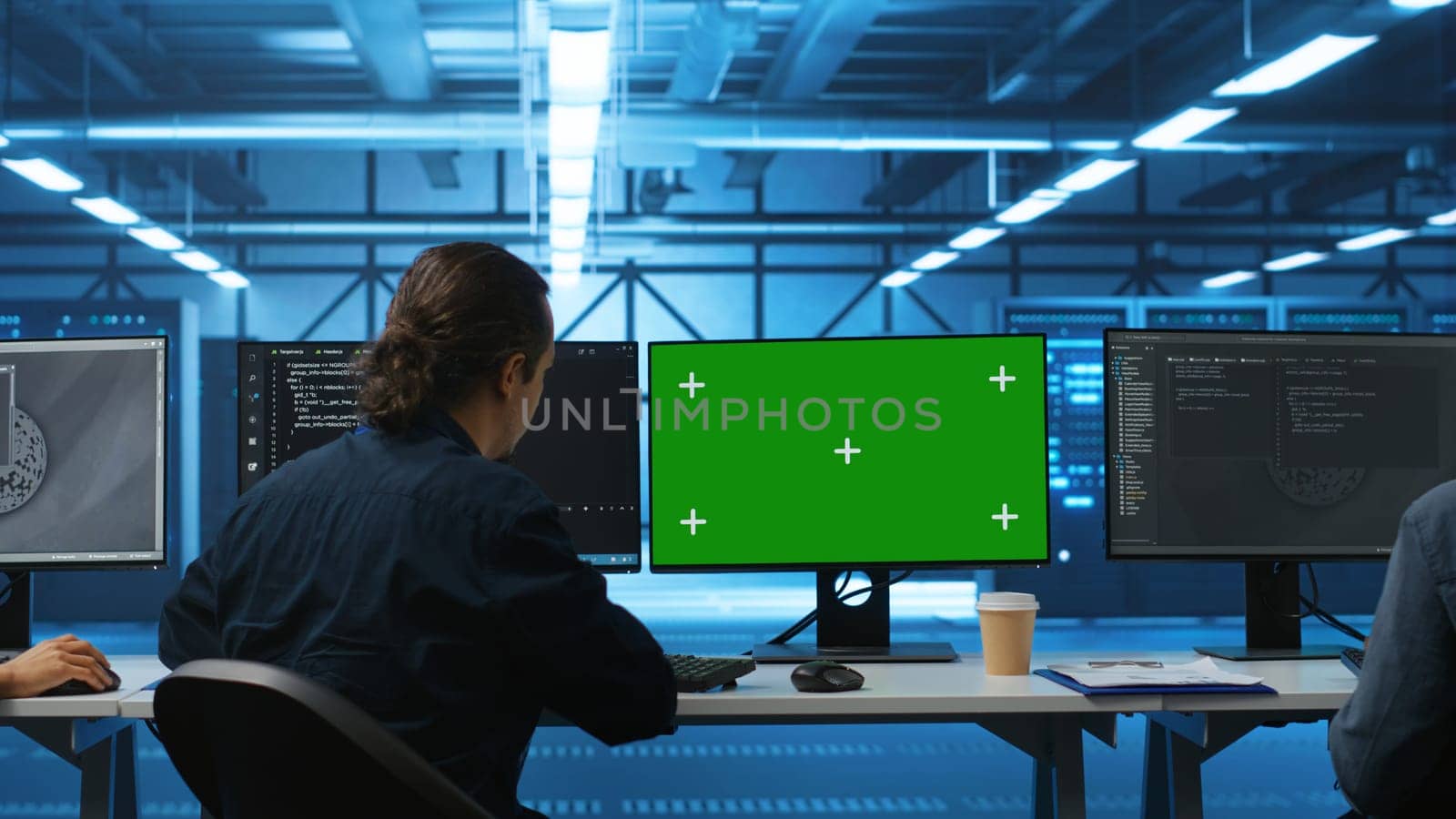 IT support workers in data center coding on green screen computers, upgrading equipment. Multiethnic team of engineers at PC desk overseeing server clusters using mockup monitors