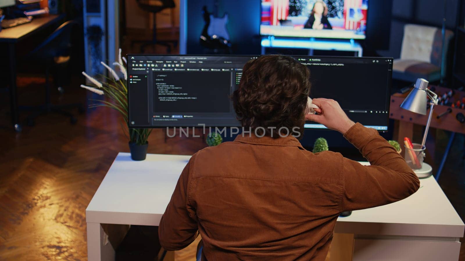 Computer scientist at home office desk writes binary code scripts and drinks from mug of coffee. IT expert in apartment enjoying tea while using programming to safeguard consumer data, camera B