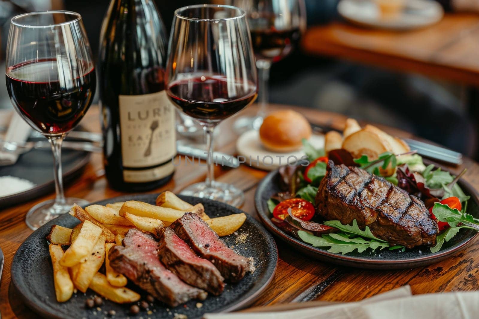 A plate of steak and fries sits on a table with a bottle of wine. The plate is topped with a salad and a glass of wine. Scene is relaxed and indulgent