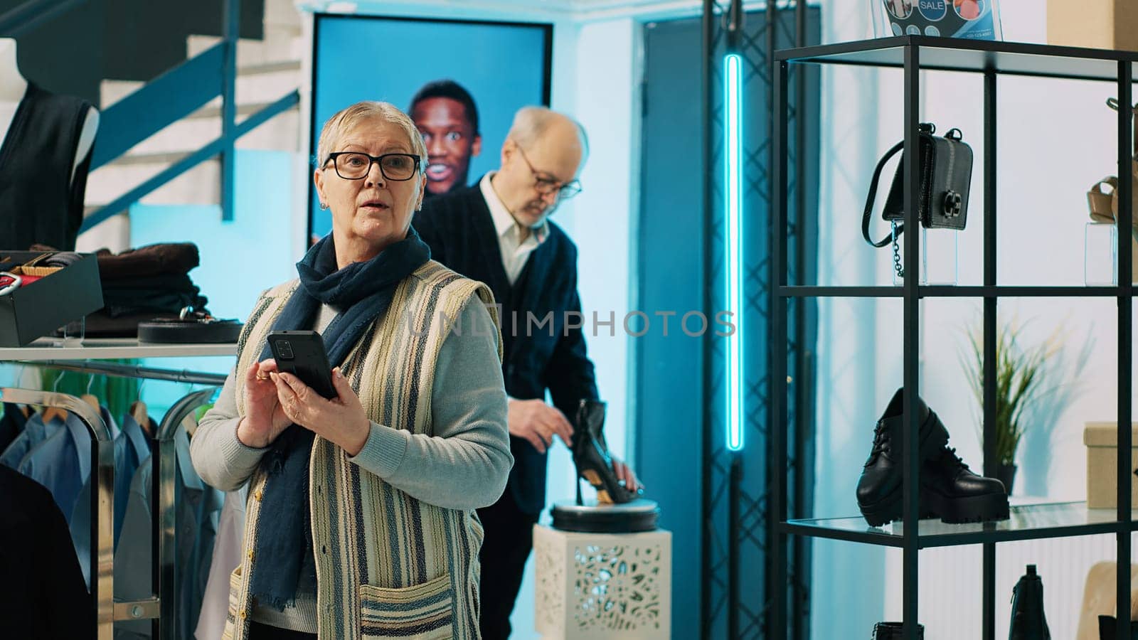 Elderly woman checking website stock to find items in store at mall, shopping for the new designer collection. Customer using smartphone app and looking for formal clothing line. Camera A.