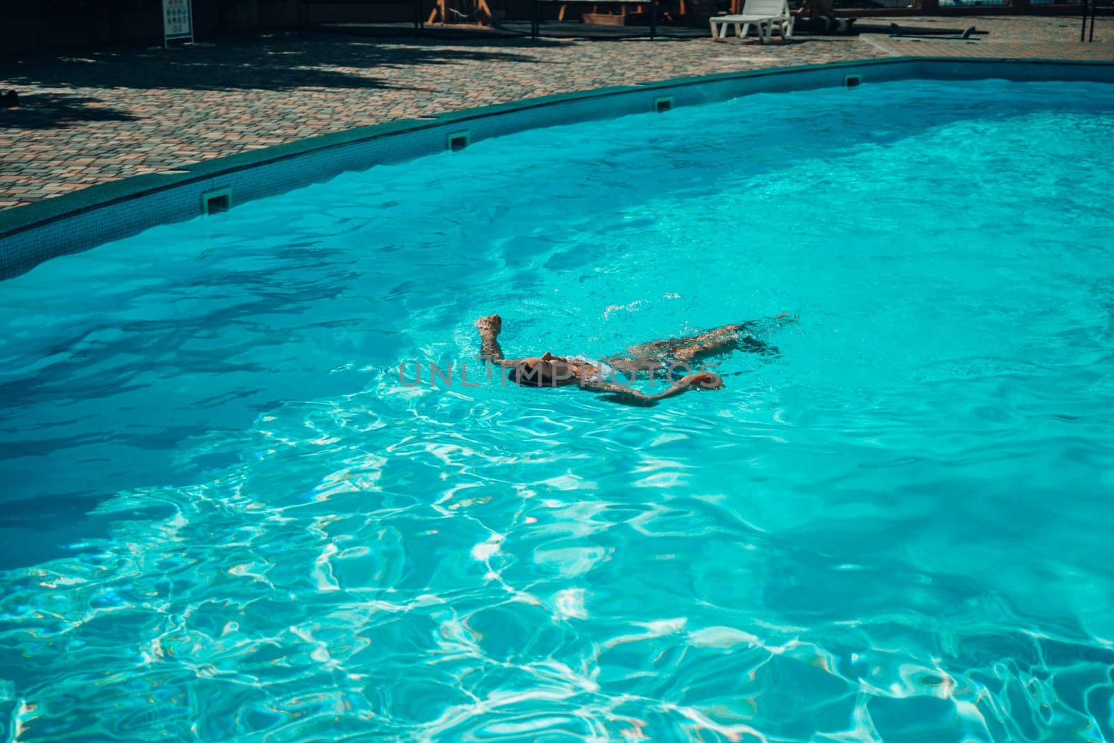A woman is swimming in a pool. The pool is surrounded by a fence and has a playground in the background