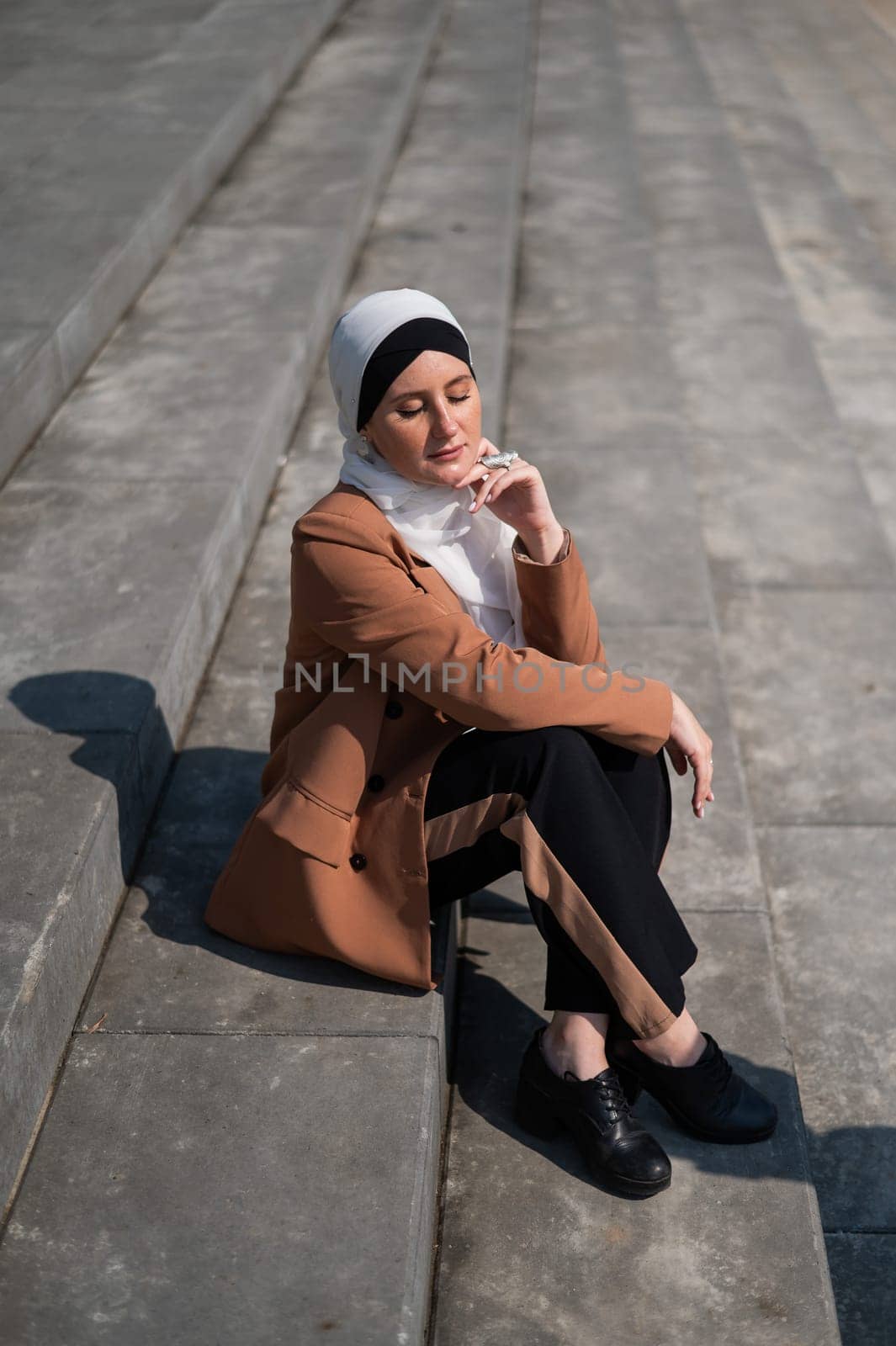 A young woman dressed in a hijab and a business suit is sitting on the stairs. by mrwed54
