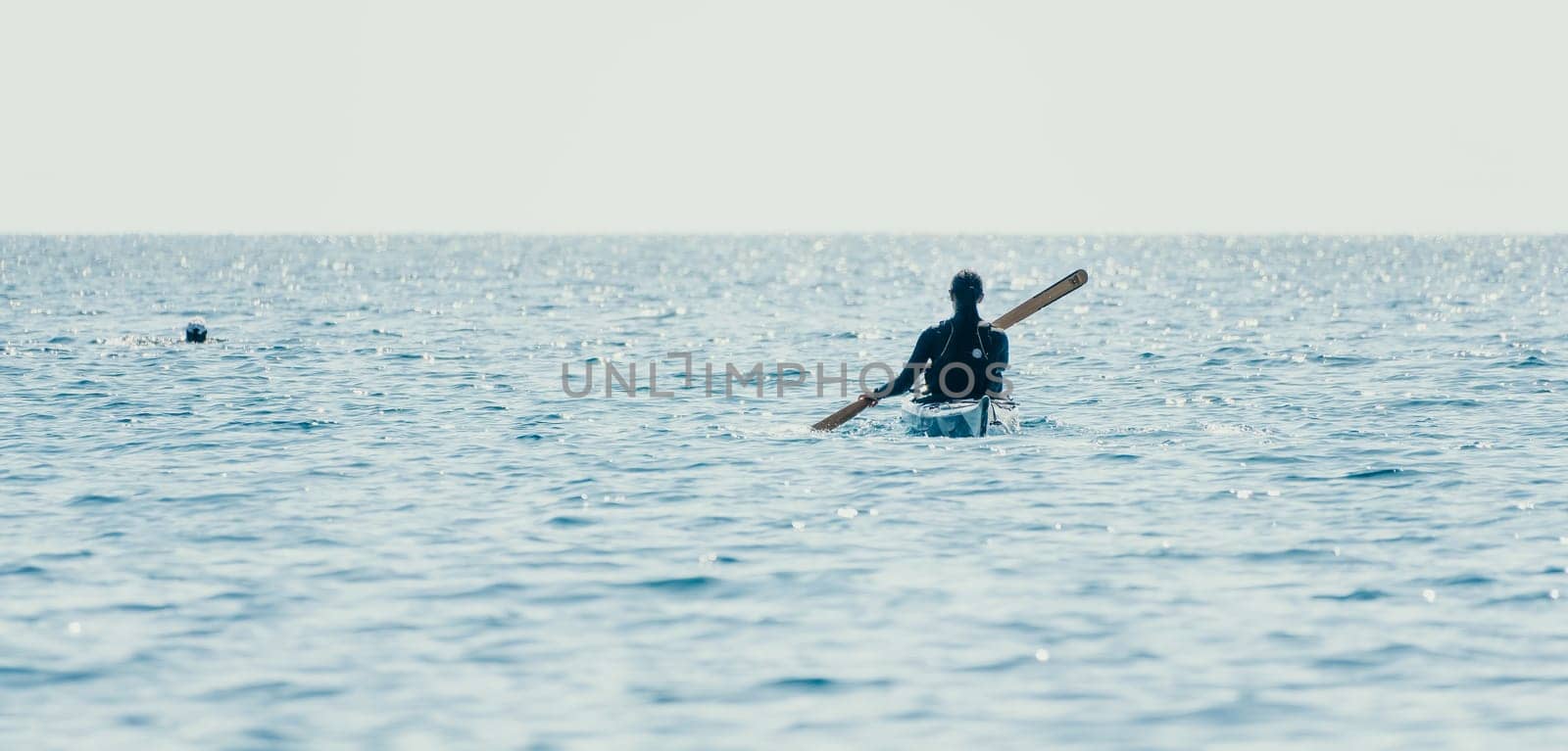 Happy smiling woman in kayak on ocean, paddling with wooden oar. Calm sea water and horizon in background