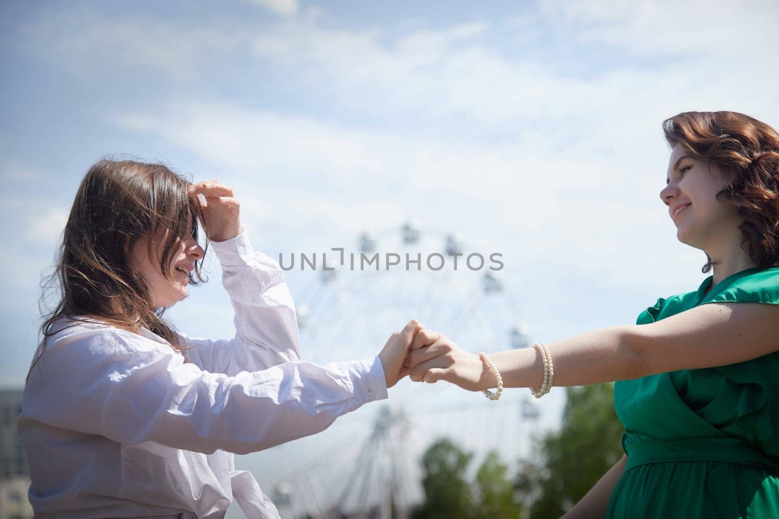 Happy Girls Enjoying Summer Day Together in the Park. Two young women stand on a platform in a park under a bright summer sky, smiling and relaxed