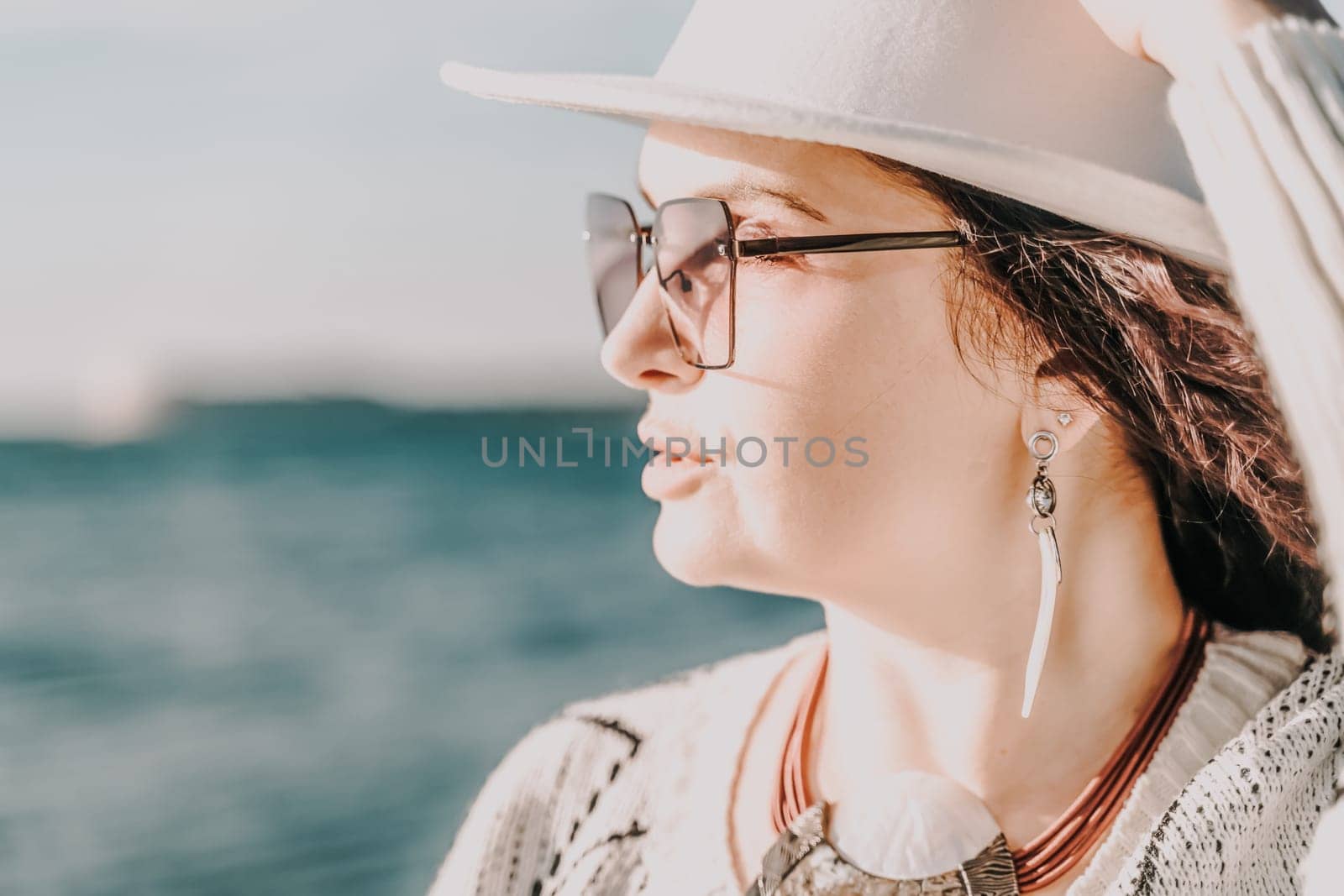 Portrait of a curly haired woman in a white hat and glasses on the background of the sea