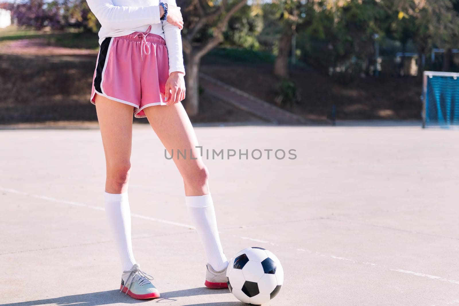 legs of an unrecognizable woman next to a soccer ball ready to play in a urban football court, concept of sport and active lifestyle, copy space for text