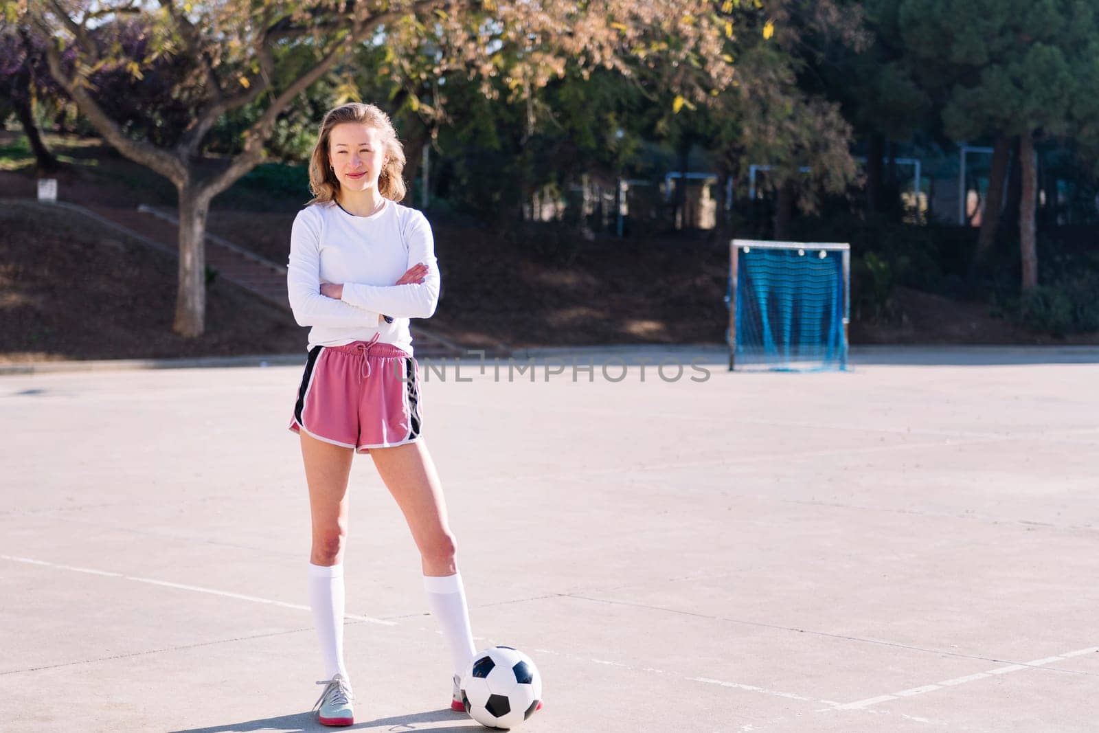 smiling young caucasian woman next to a soccer ball ready to play in a urban football court, concept of sport and active lifestyle, copy space for text