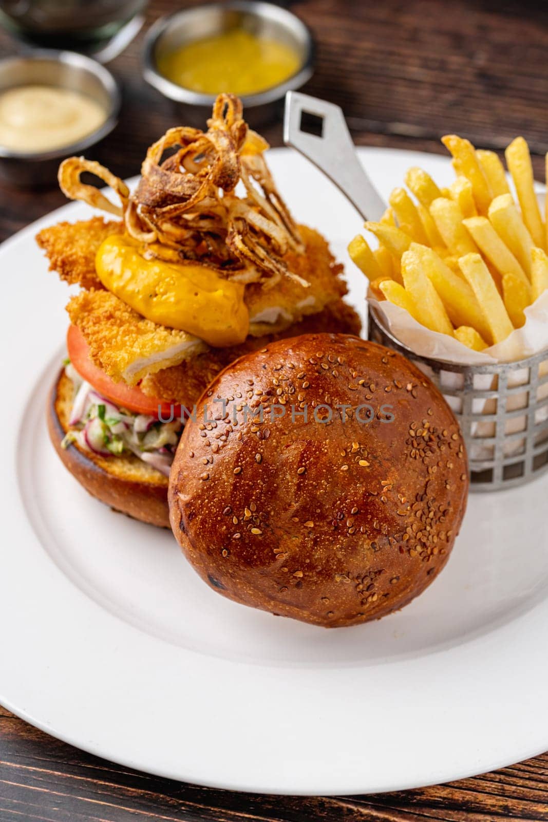 Chicken burger served with fries and sauces on a white porcelain plate