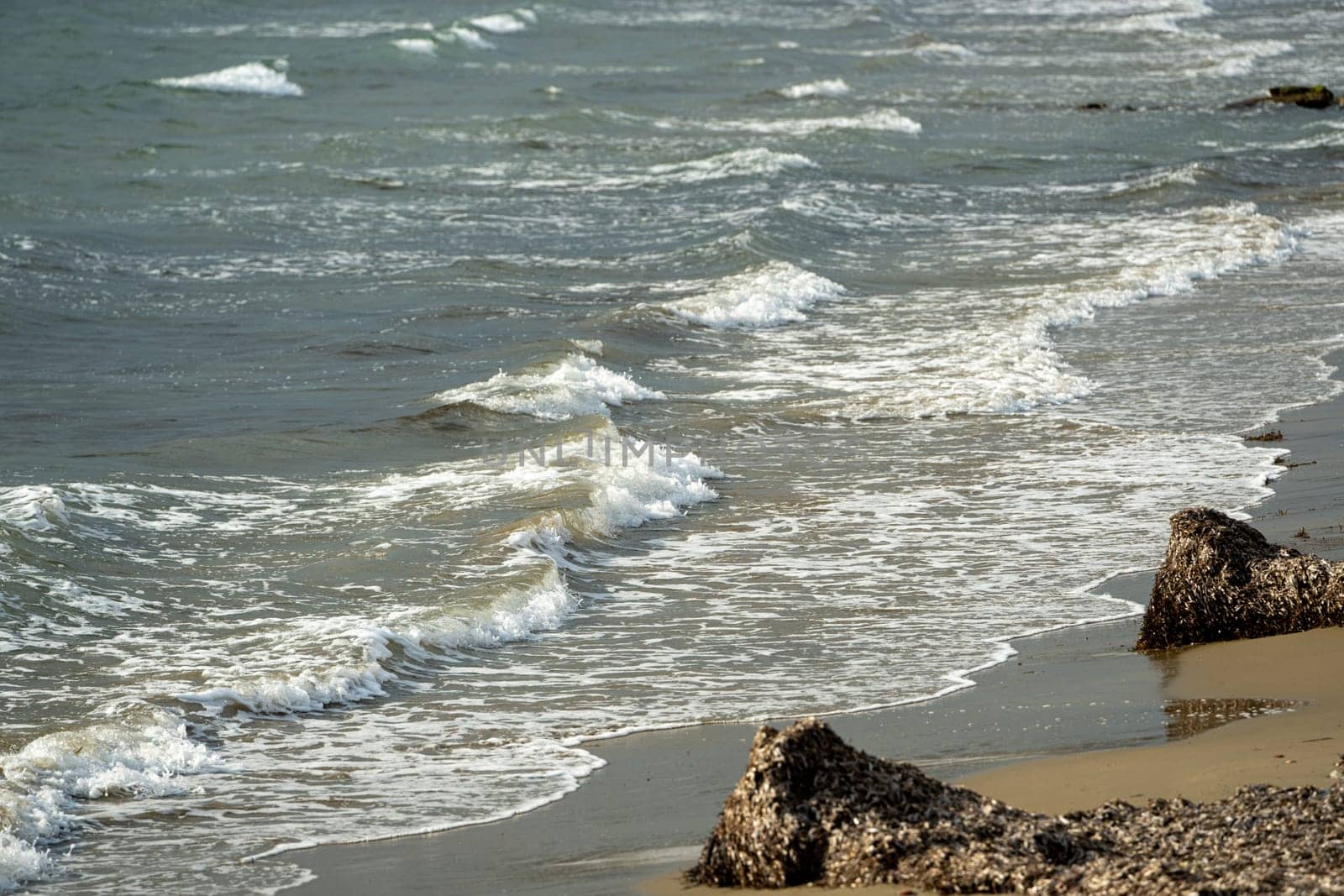 View from below of sandy beach and waves at sunset by Sonat