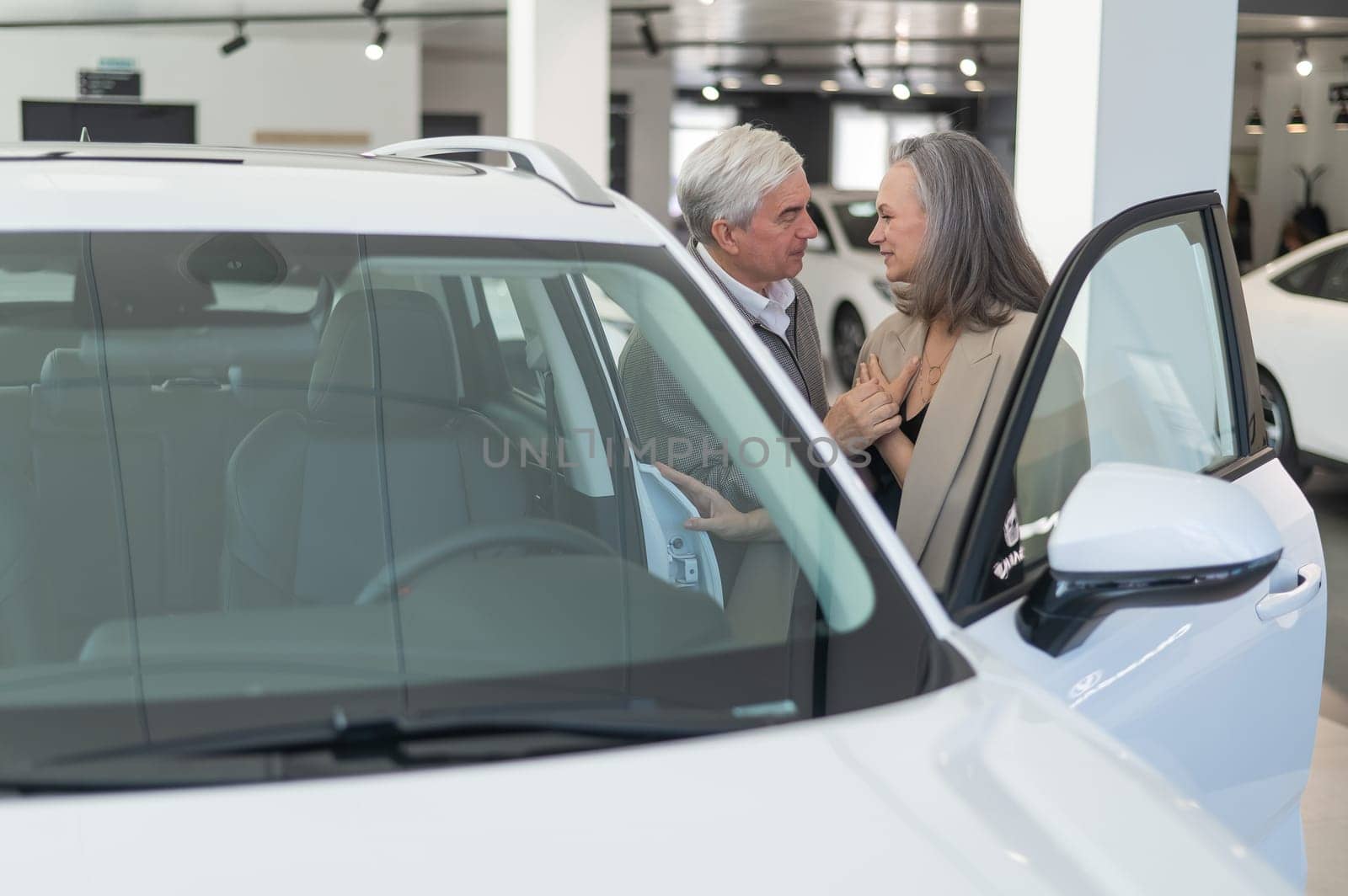 An elderly Caucasian couple chooses a new car at a car dealership