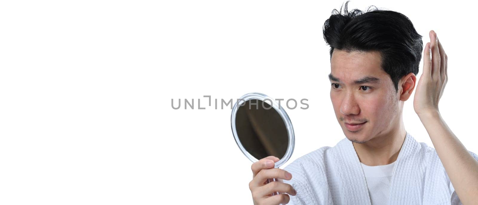 Young Asian man looking at mirror and styling his hair over white background.