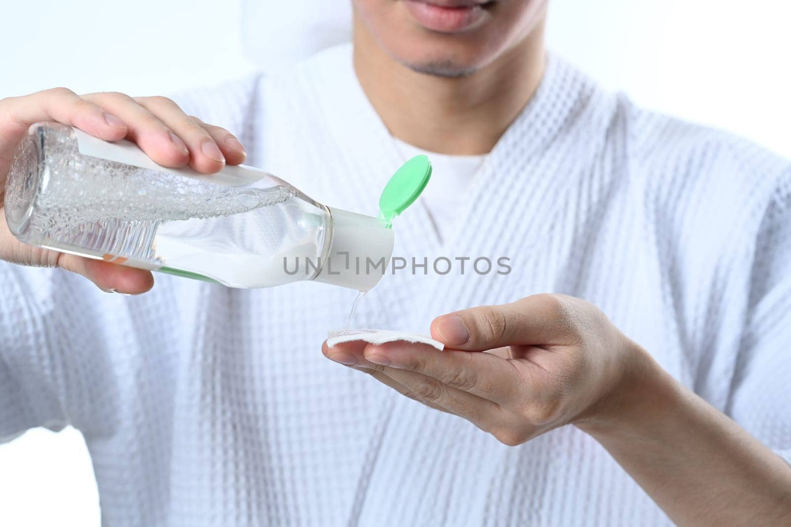 Man applying toner on cotton pad on white background. Male beauty and skincare concept.
