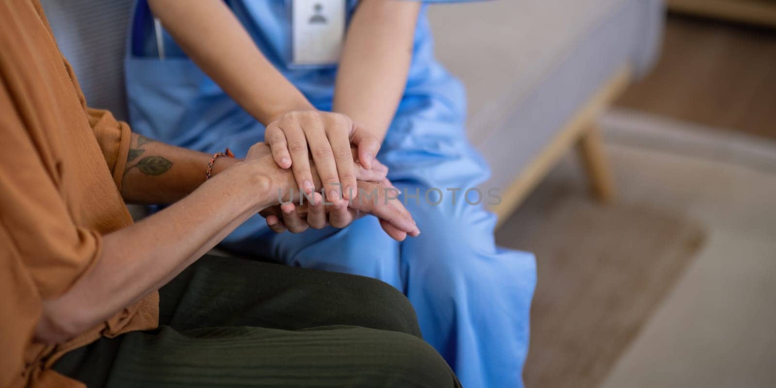 Close up of an Asian caregiver holding hands with an elderly woman at home, emphasizing compassion and support