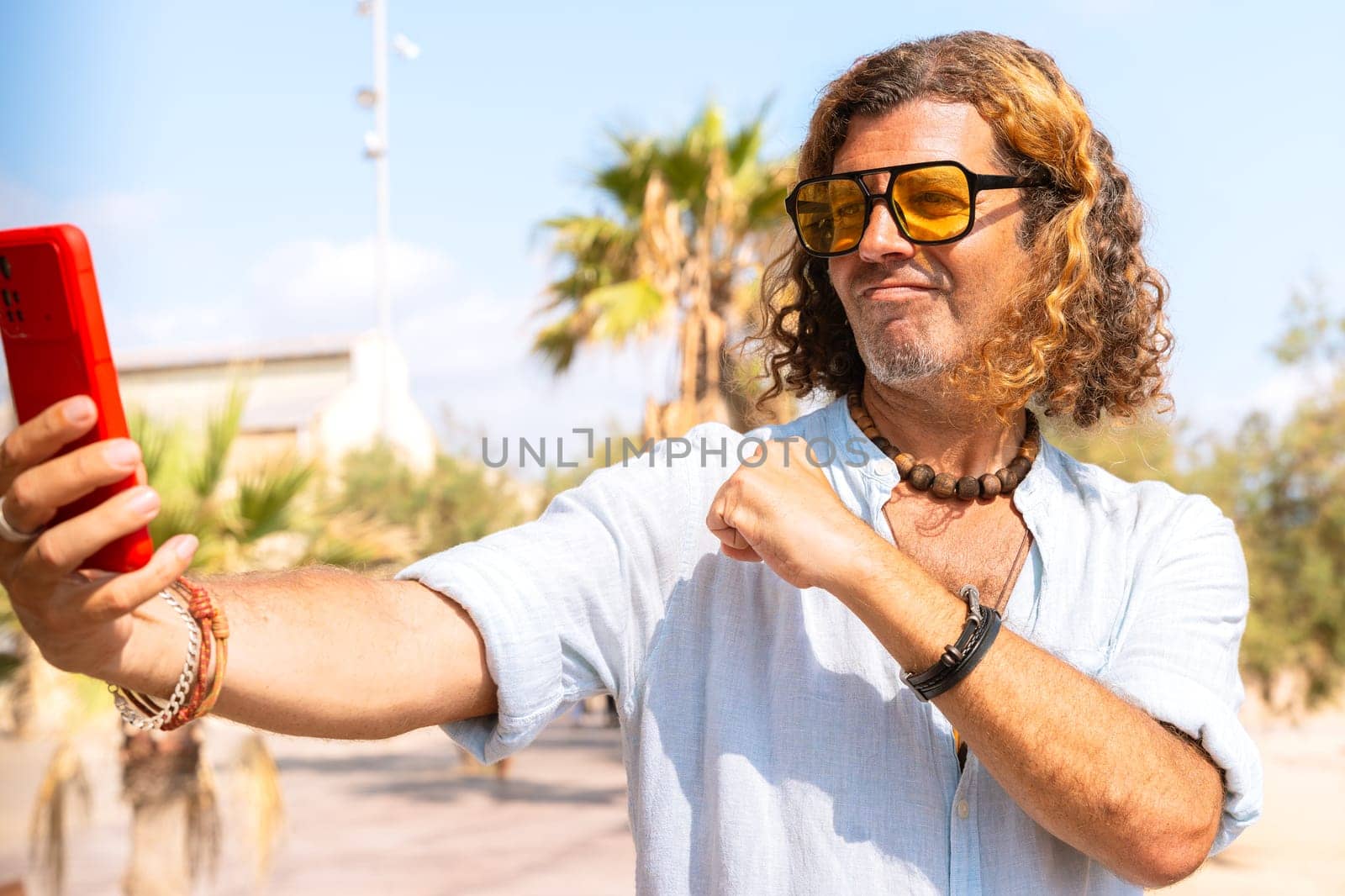 Happy average adult man wearing sunglasses on beach vacation taking a selfie for his family with his smartphone.