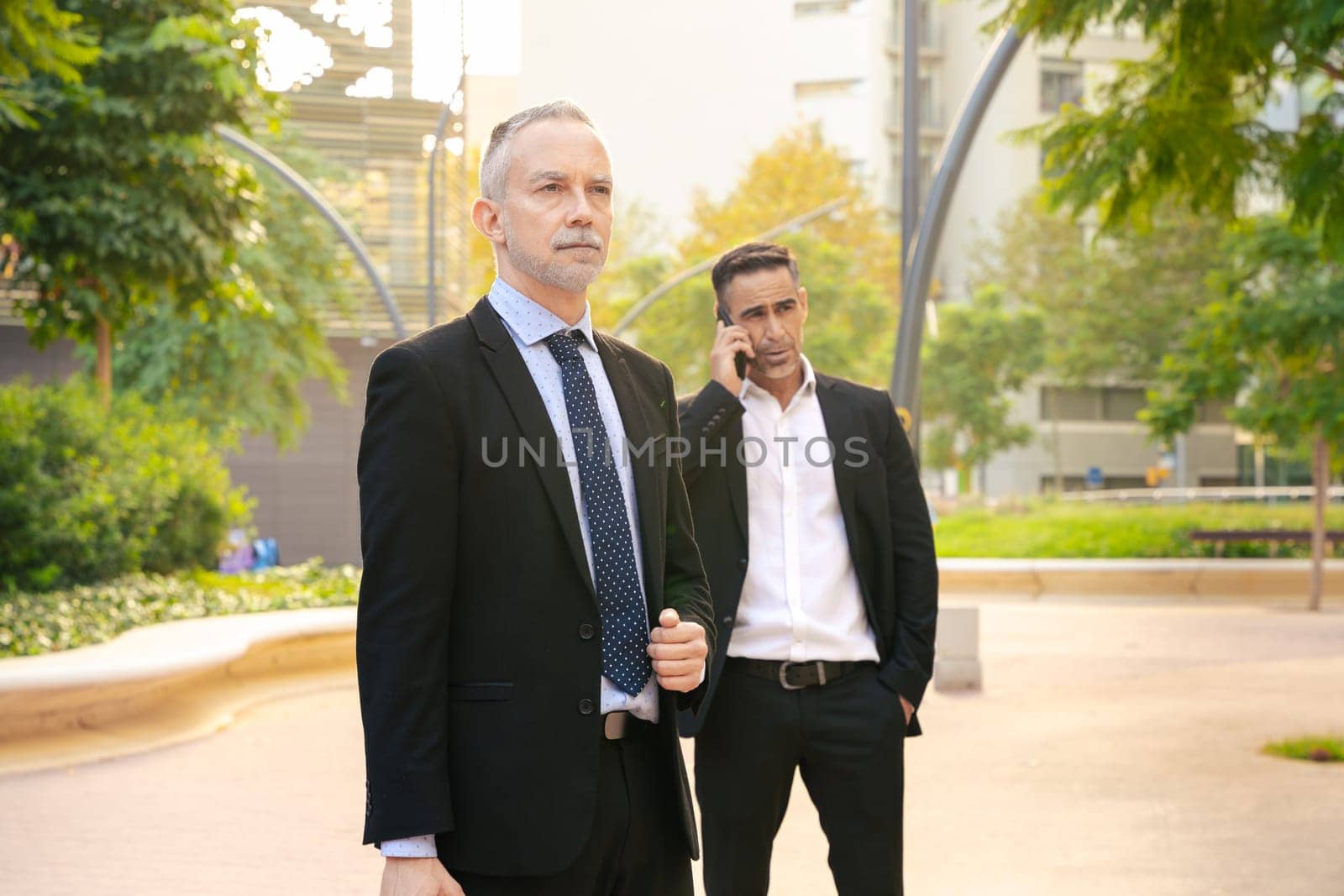 Two businessmen at the exit of a meeting talking on smartphone. by mariaphoto3