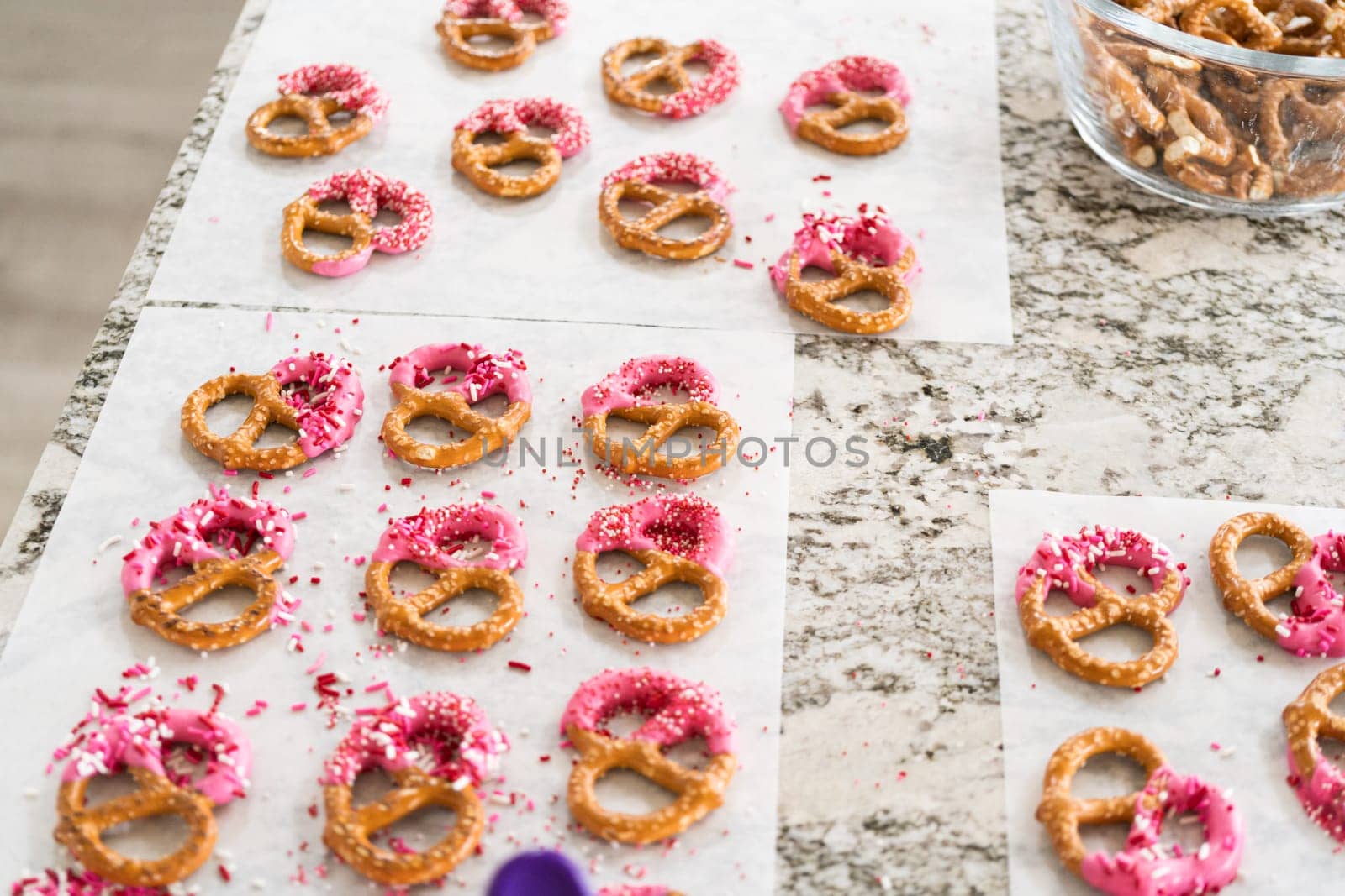 Freshly dipped and still glistening, these crunchy pretzels are lovingly adorned with pink chocolate and a scattering of colorful sprinkles, promising a feast for the senses.