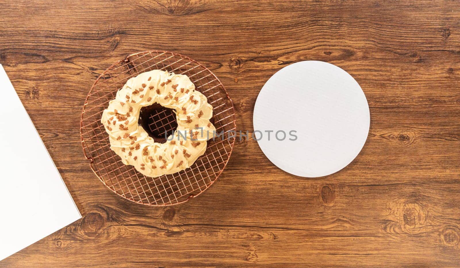 Flat lay. Carefully placing the gingerbread bundt cake, adorned with salted caramel frosting and gingerbread sprinkles, into a white paper bundt cake box with a clear window for gifting.