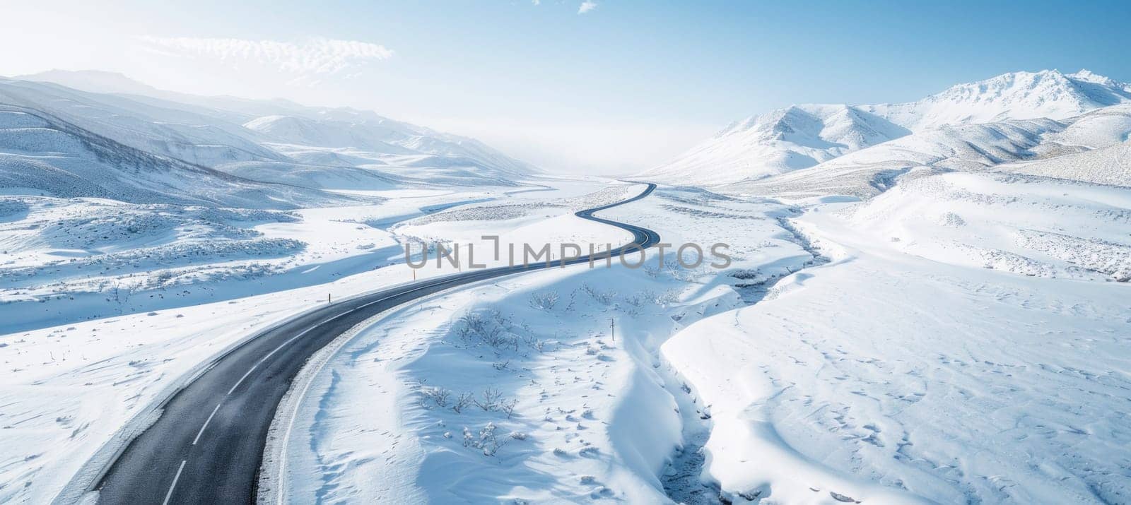 This is an aerial view of a snowcovered road meandering through hills, capturing the winter charm of nature