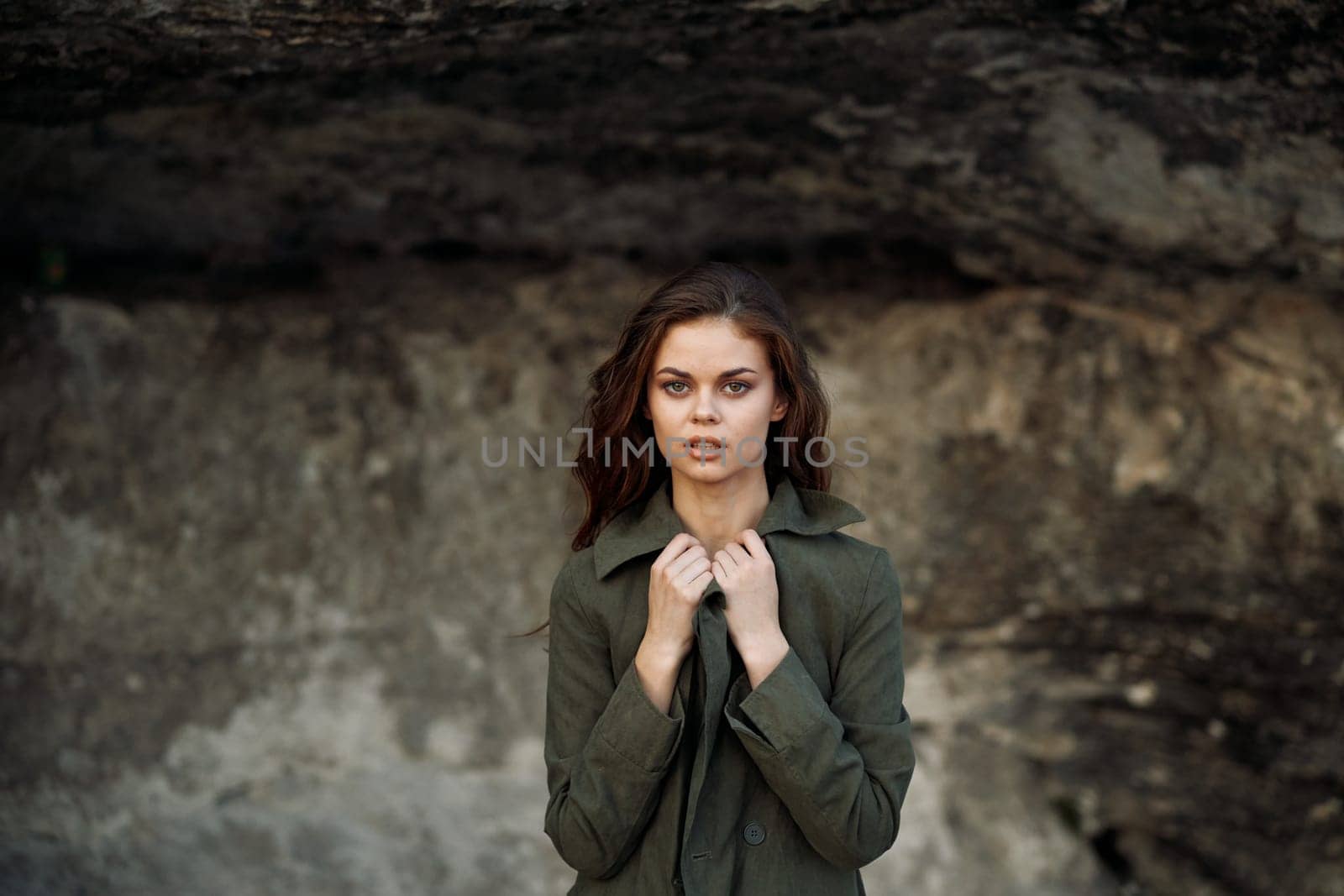 Serene woman in green jacket standing in contemplation before textured rock wall by Vichizh