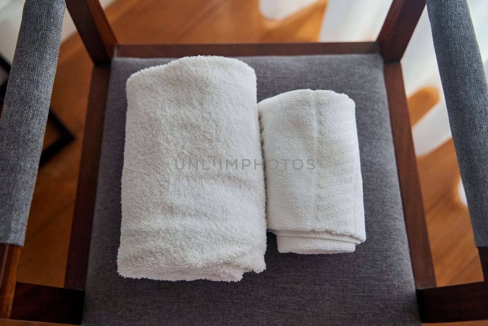 A pair of rolled hardwood towels are placed on a wooden chair, resembling a spiral pattern. The towels sit in a rectangular shape on the chair in a room with wooden flooring