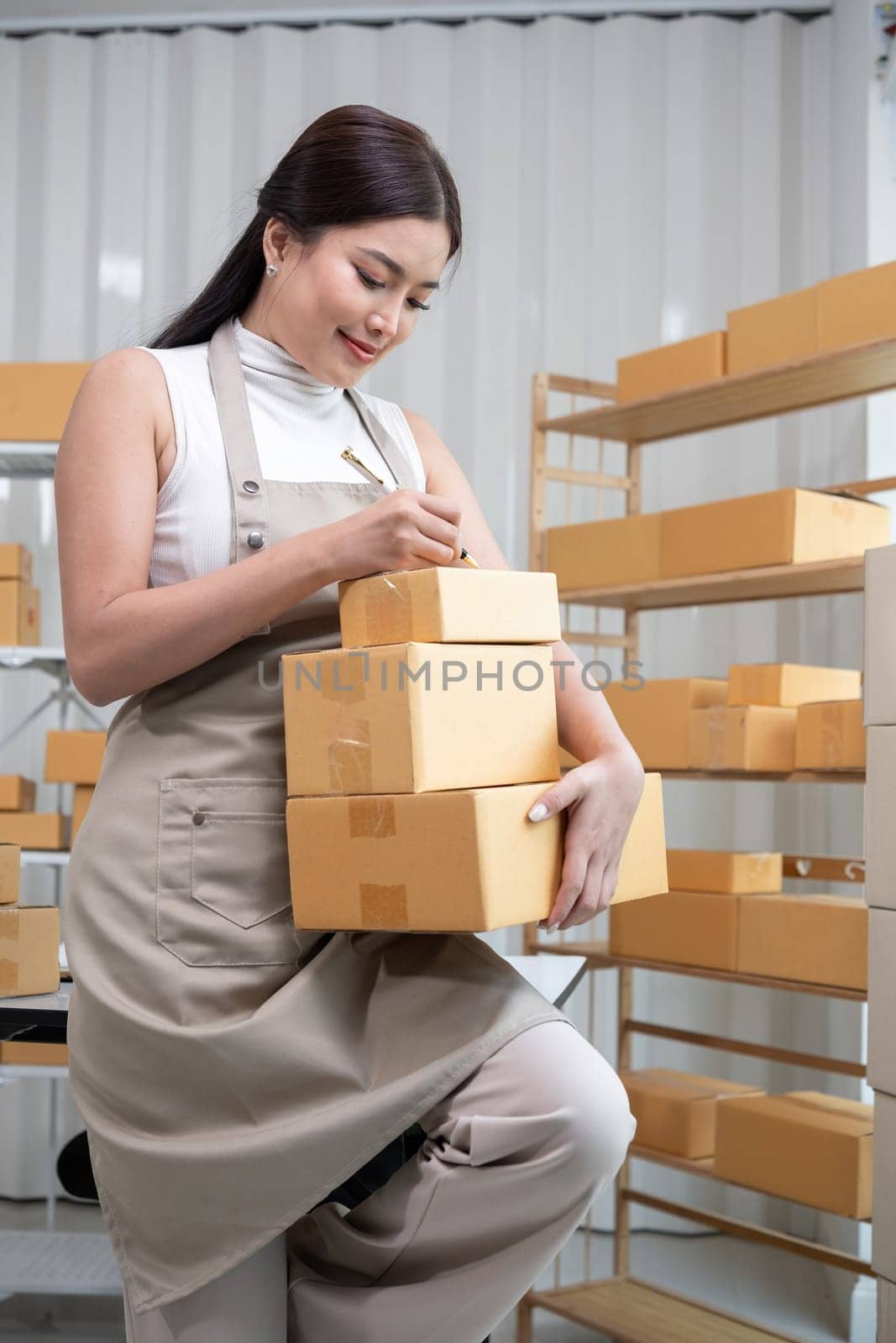 Woman Packing Boxes of Merchandise for Online Sales in a Modern Warehouse Setting by wichayada