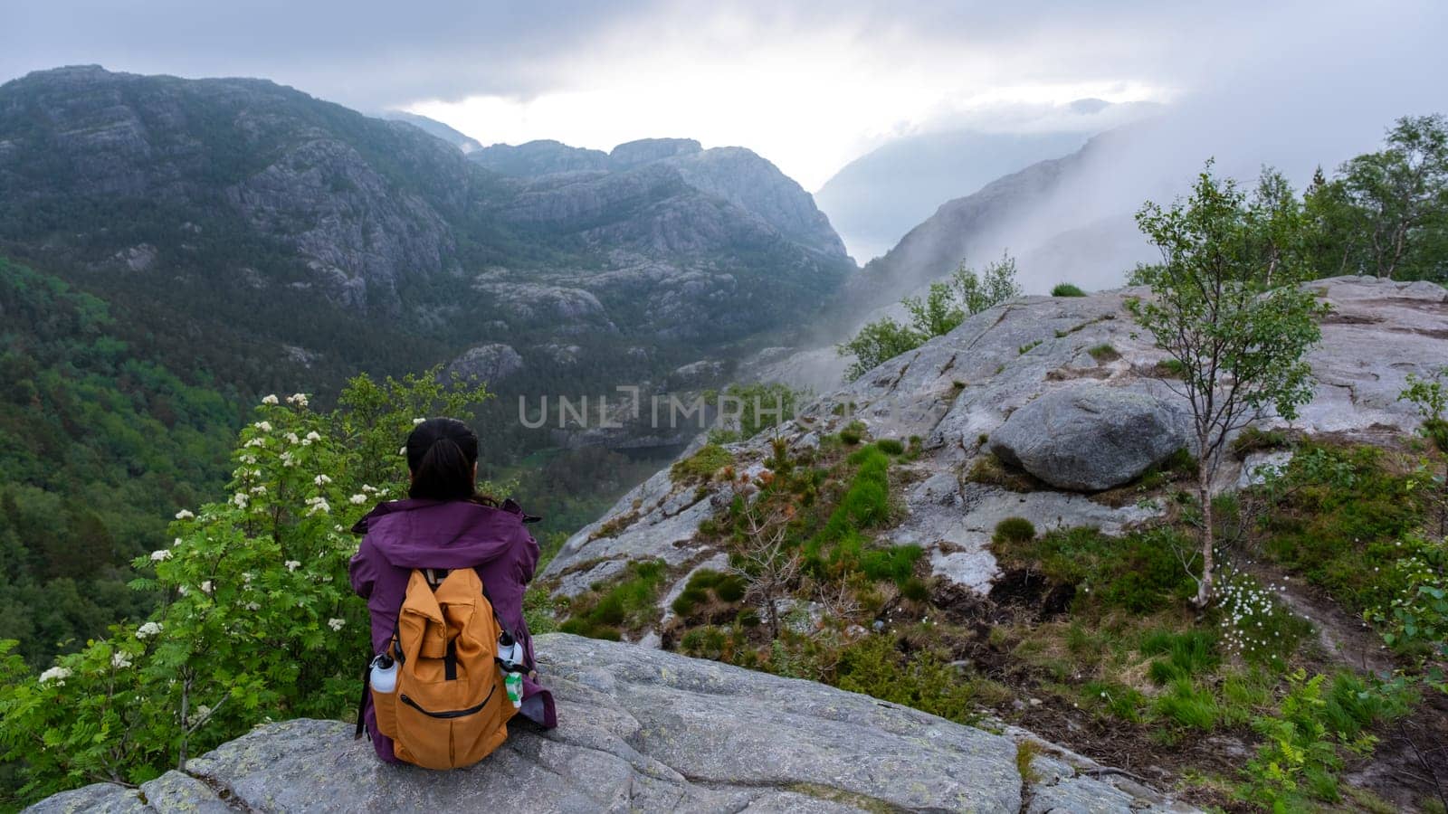 A hiker pauses on a rocky outcrop, taking in the breathtaking view of the Norwegian mountains shrouded in mist. Preikestolen, Norway