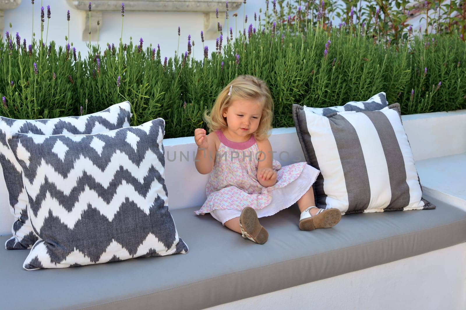 Two year old girl sits on sofa surrounded by lavender in a garden