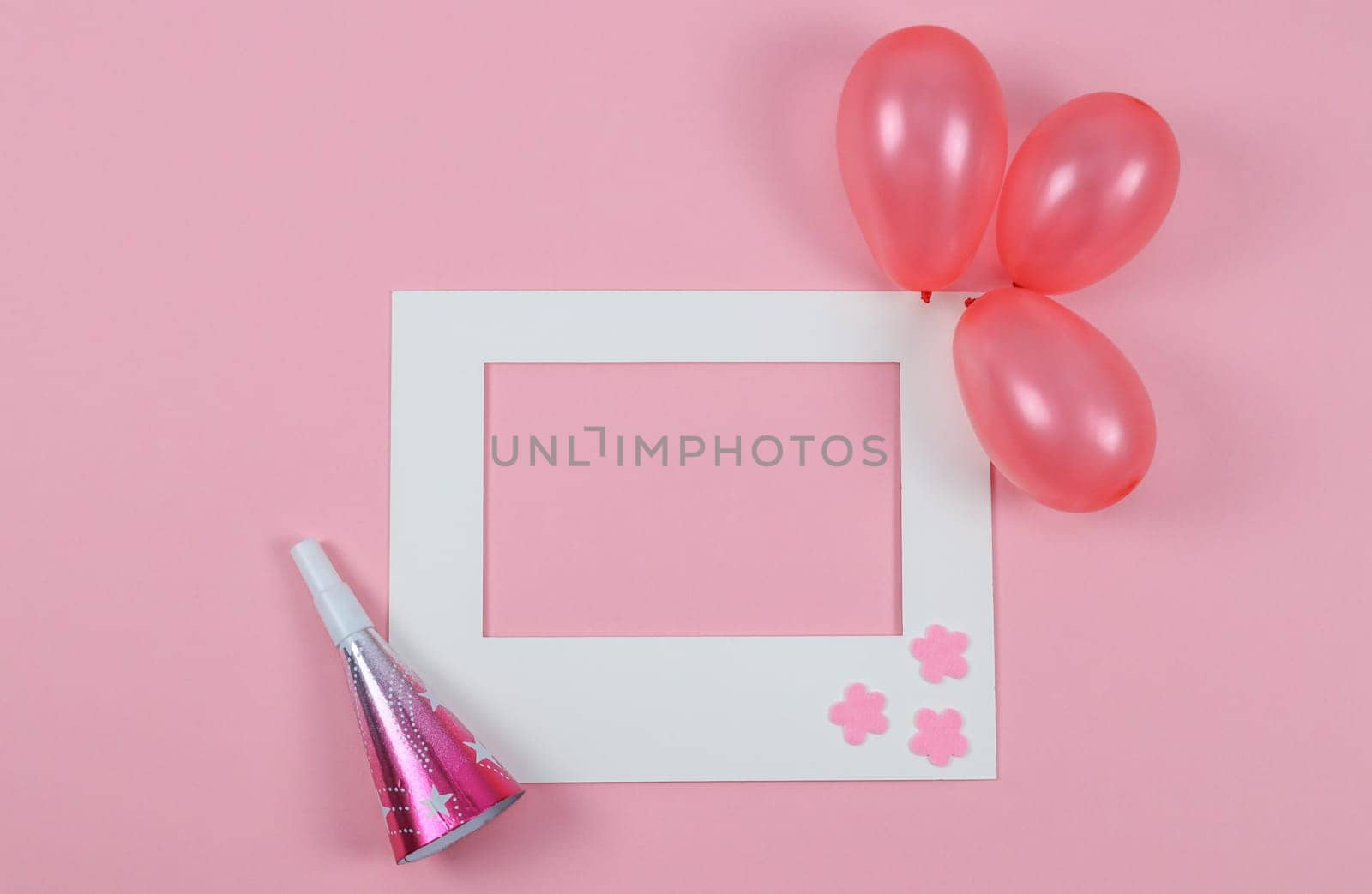 Empty paper frame, three inflated mini balls and one whistle lie on a pink background with copy space in the center, flat lay close-up.