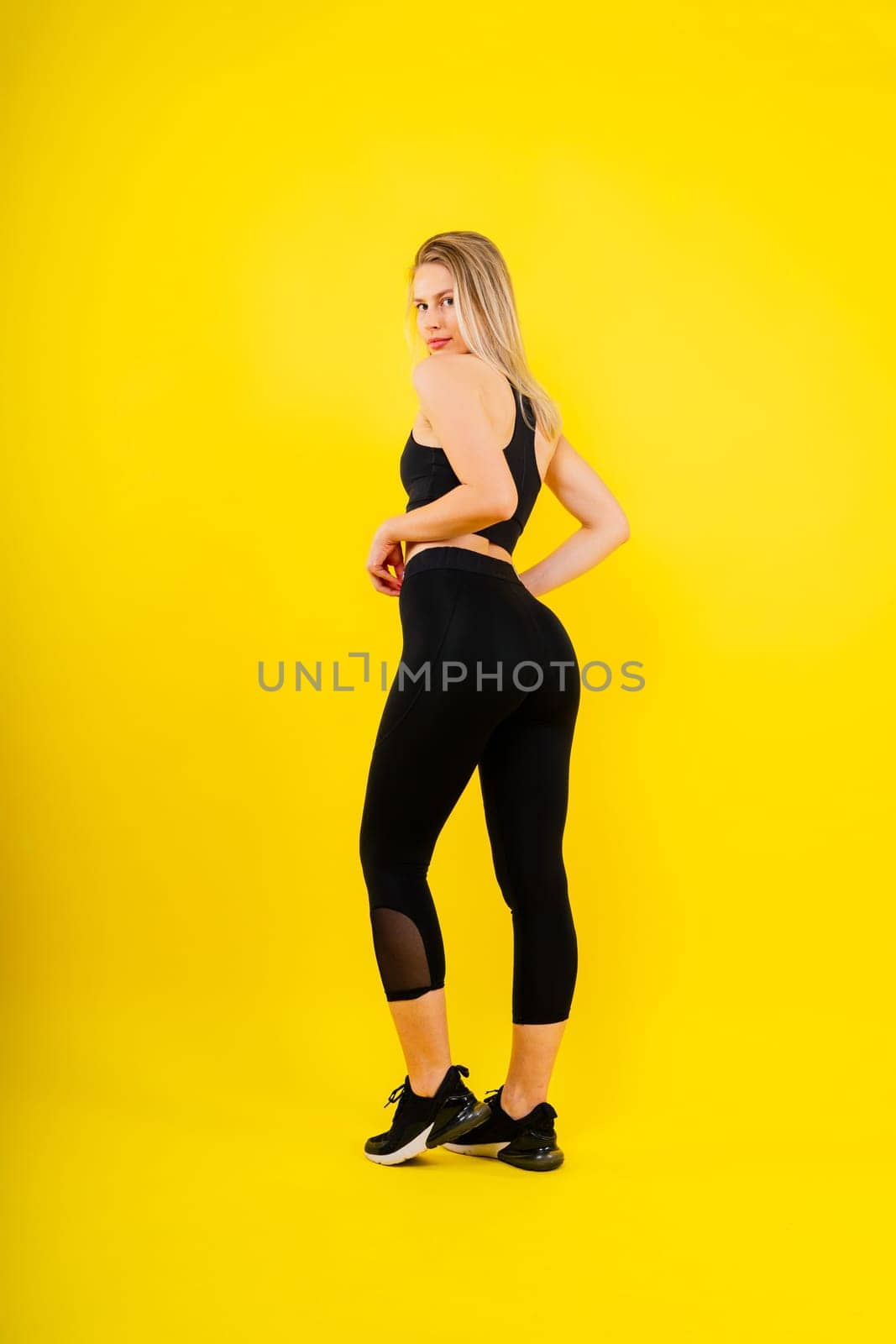 Fit sportswoman in leggings and sports bra looking away and while standing on yellow red by Zelenin