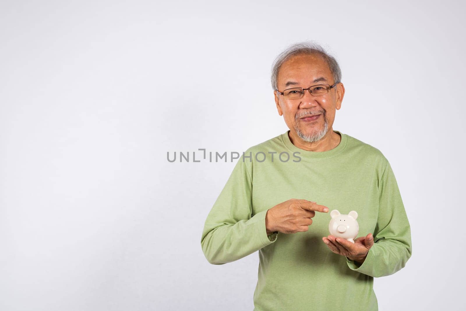 Portrait Asian older man points to a white piggy bank holding on hand studio shot isolated on white background. Concept of responsibility and financial planning, Saving money After retirement