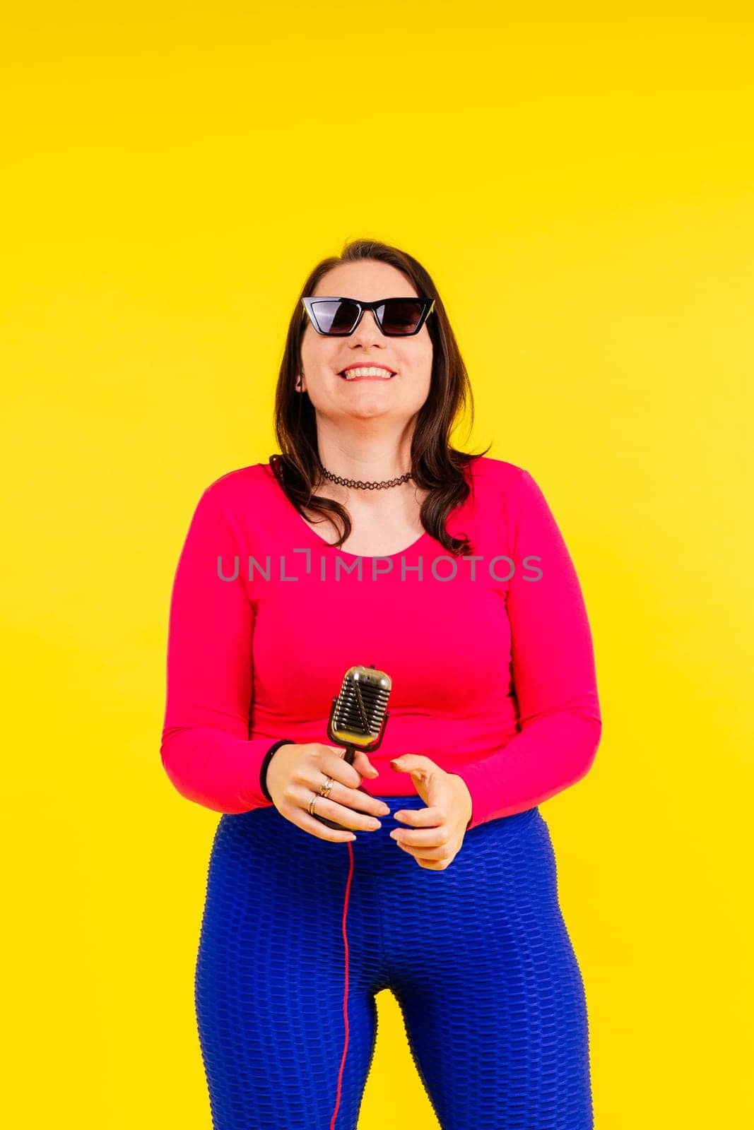 Smiling brunette woman with microphone on a colored studio background