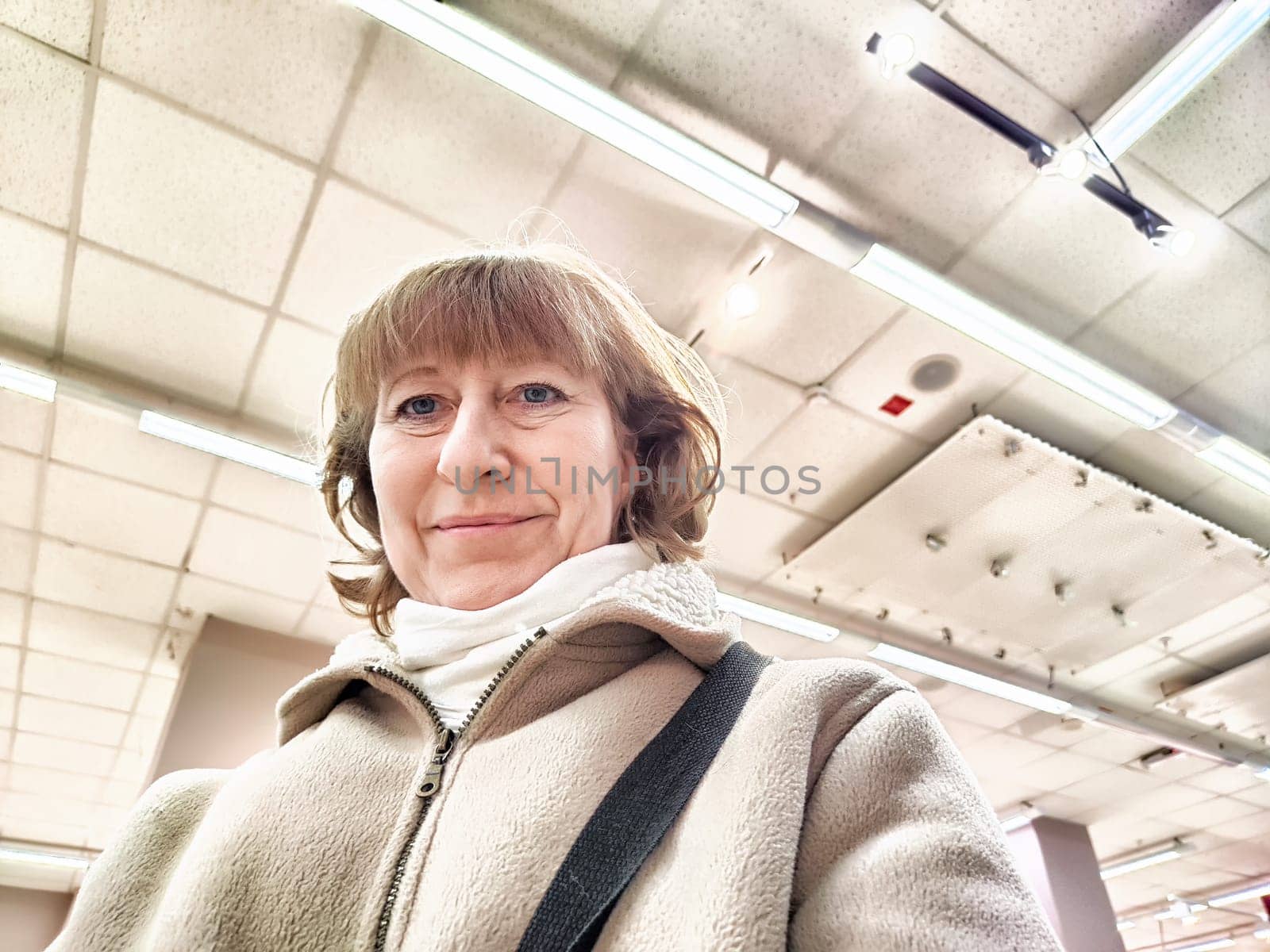 Middle-Aged Woman Captures Selfie While Shopping Indoors. Smiling adult shopper takes self-portrait during an indoor shopping trip