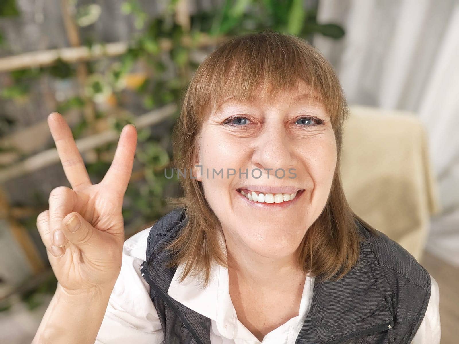 Portrait of a middle-aged woman taking selfie in a room with plants and flowers. Blogger and online streaming