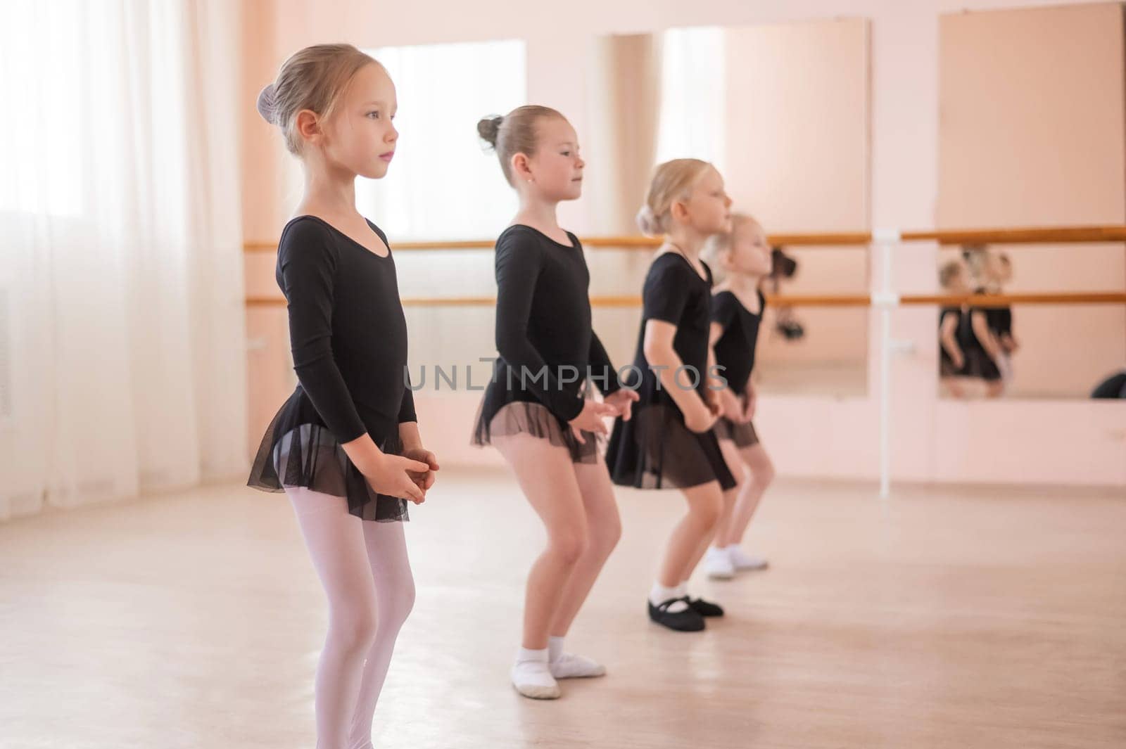 Cute little girls in black swimsuits and tutu practice ballet in class