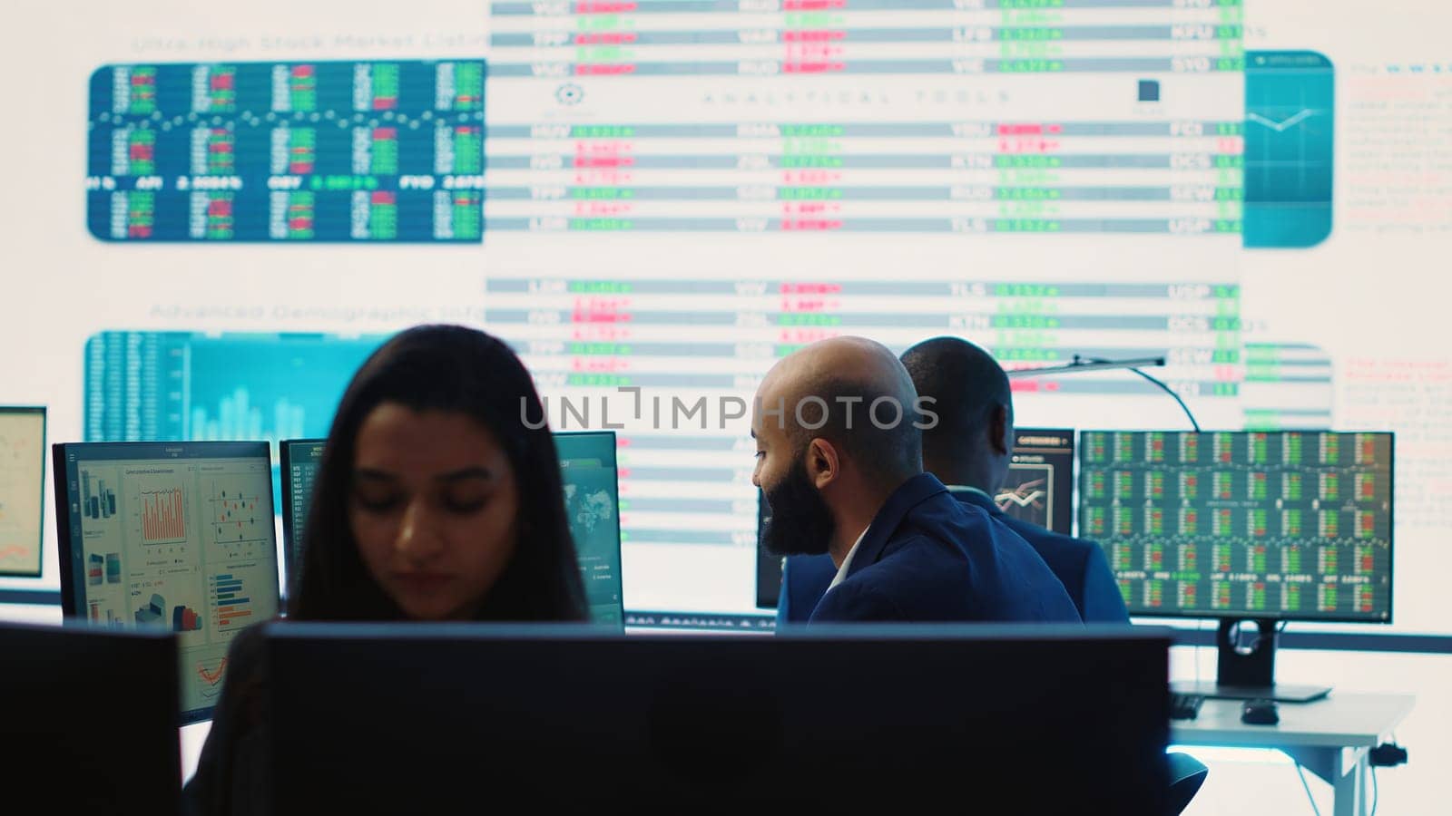 Company employees employing big data used in solving tasks, studying infographics on a huge display. Business analysts reviewing current situation numbers for annual reports. Camera A.