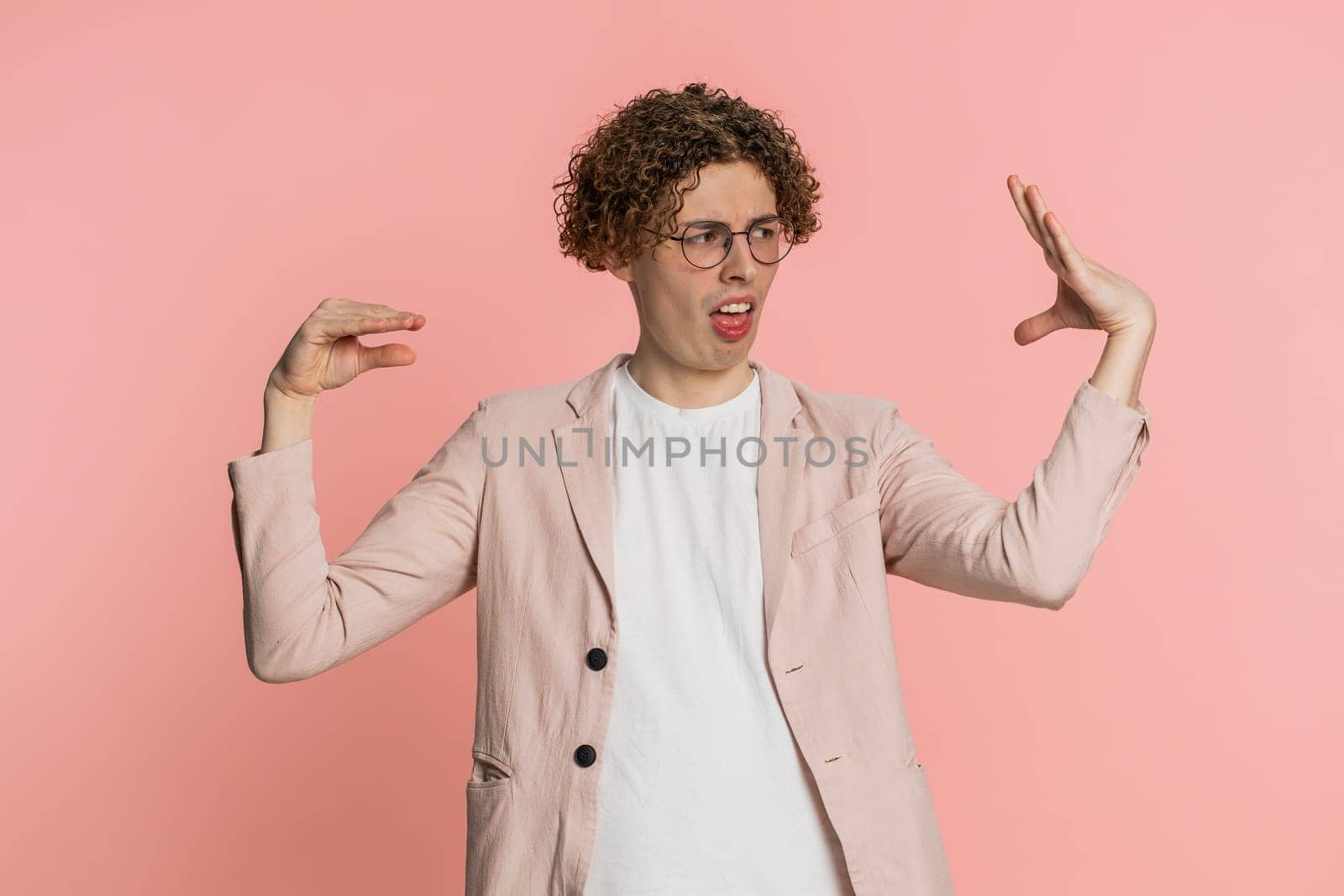 Disappointed Caucasian curly haired man in jacket showing blah blah nonsense gesture with hands, not interested in conversation, gossips, empty promises, rumors, liars. Guy isolated on pink background