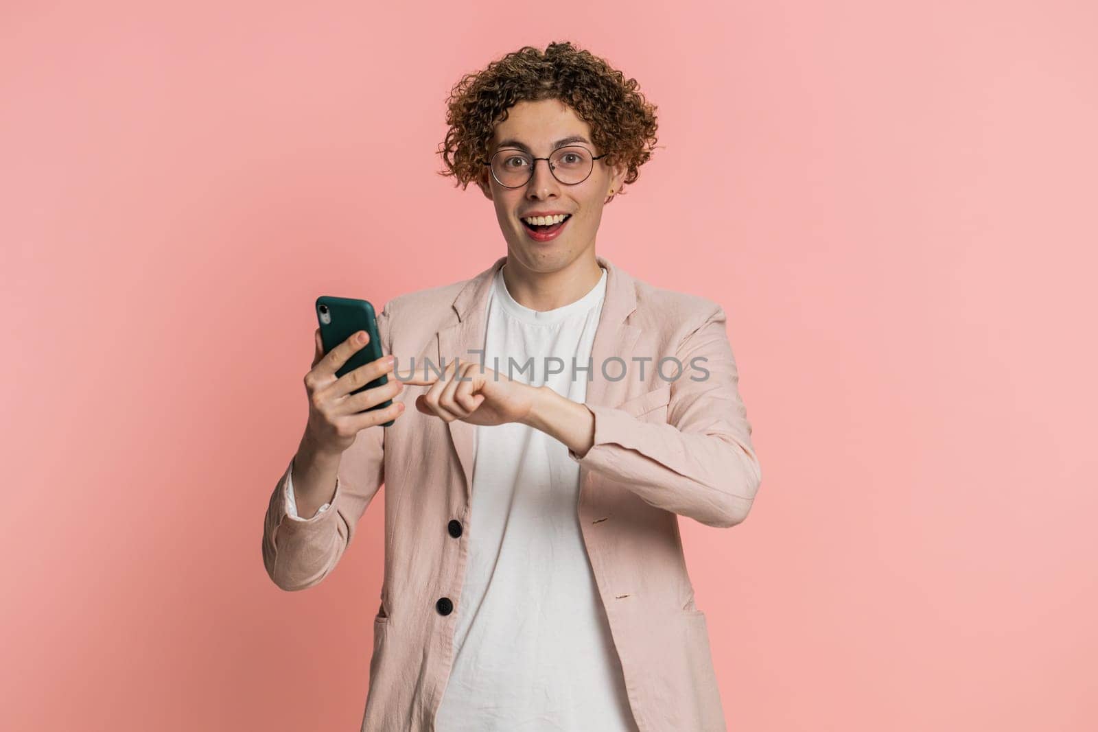 Caucasian man texting share sms messages content on smartphone social media applications online, watching relax movie browsing. Young guy uses mobile phone smile isolated on pink background indoors