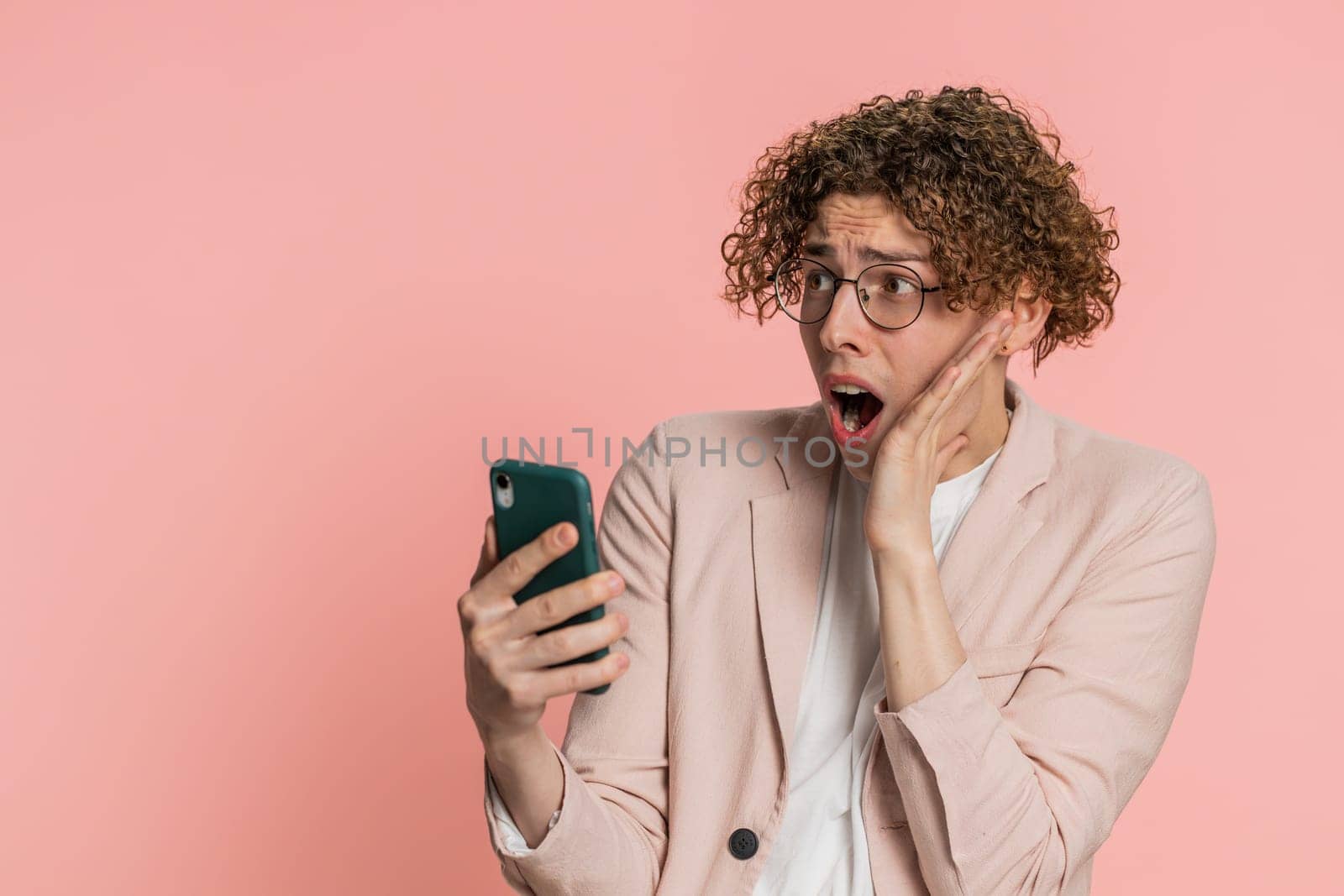 Upset sad Caucasian man use smartphone typing browsing, play game, loses, surprised by sudden lottery results bad fortune loss fail unlucky news. Handsome attractive guy isolated on pink background