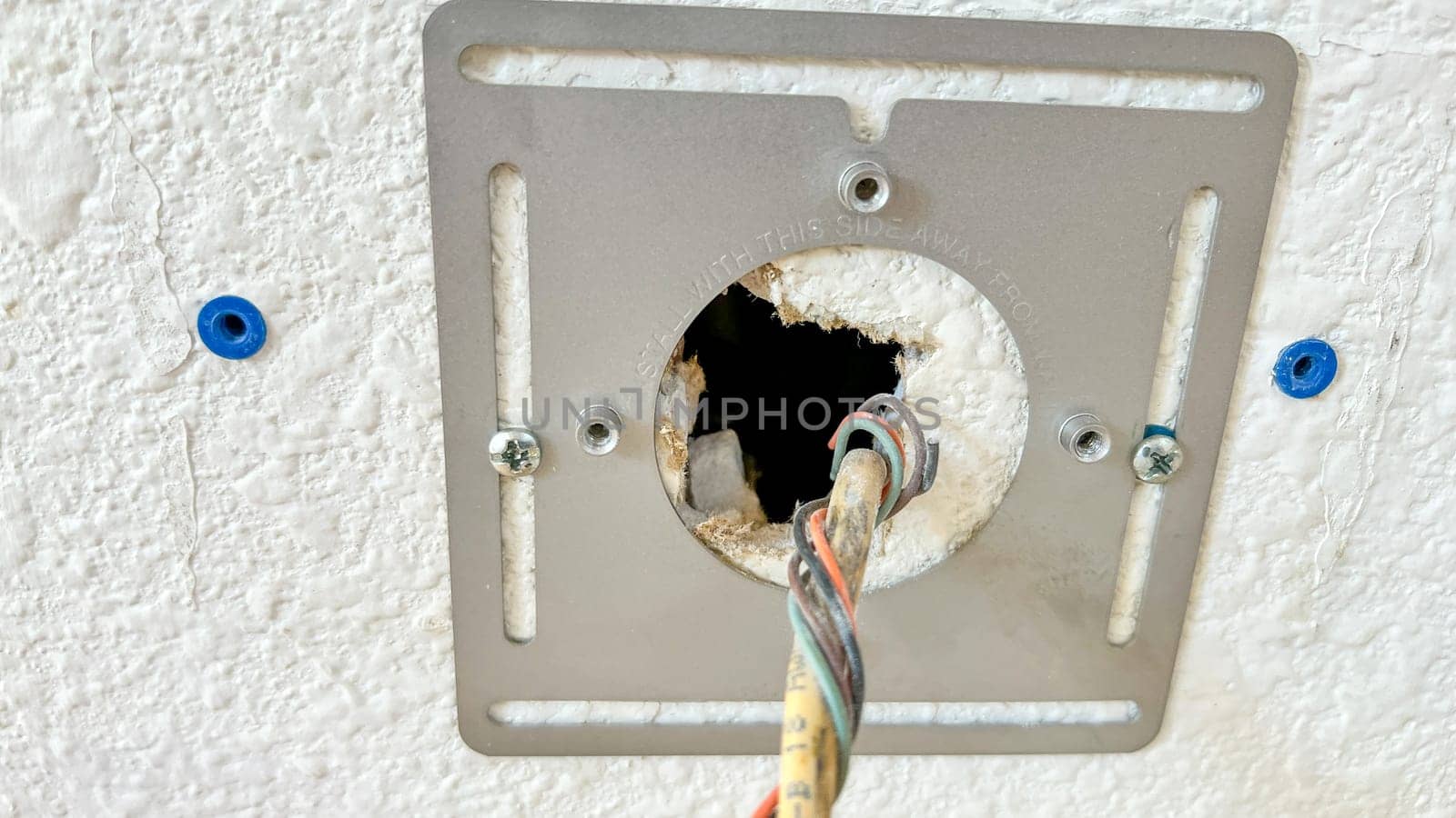 Close-up image of electrical wiring being installed through a wall plate. The exposed wires and mounting hardware are visible against the textured wall.