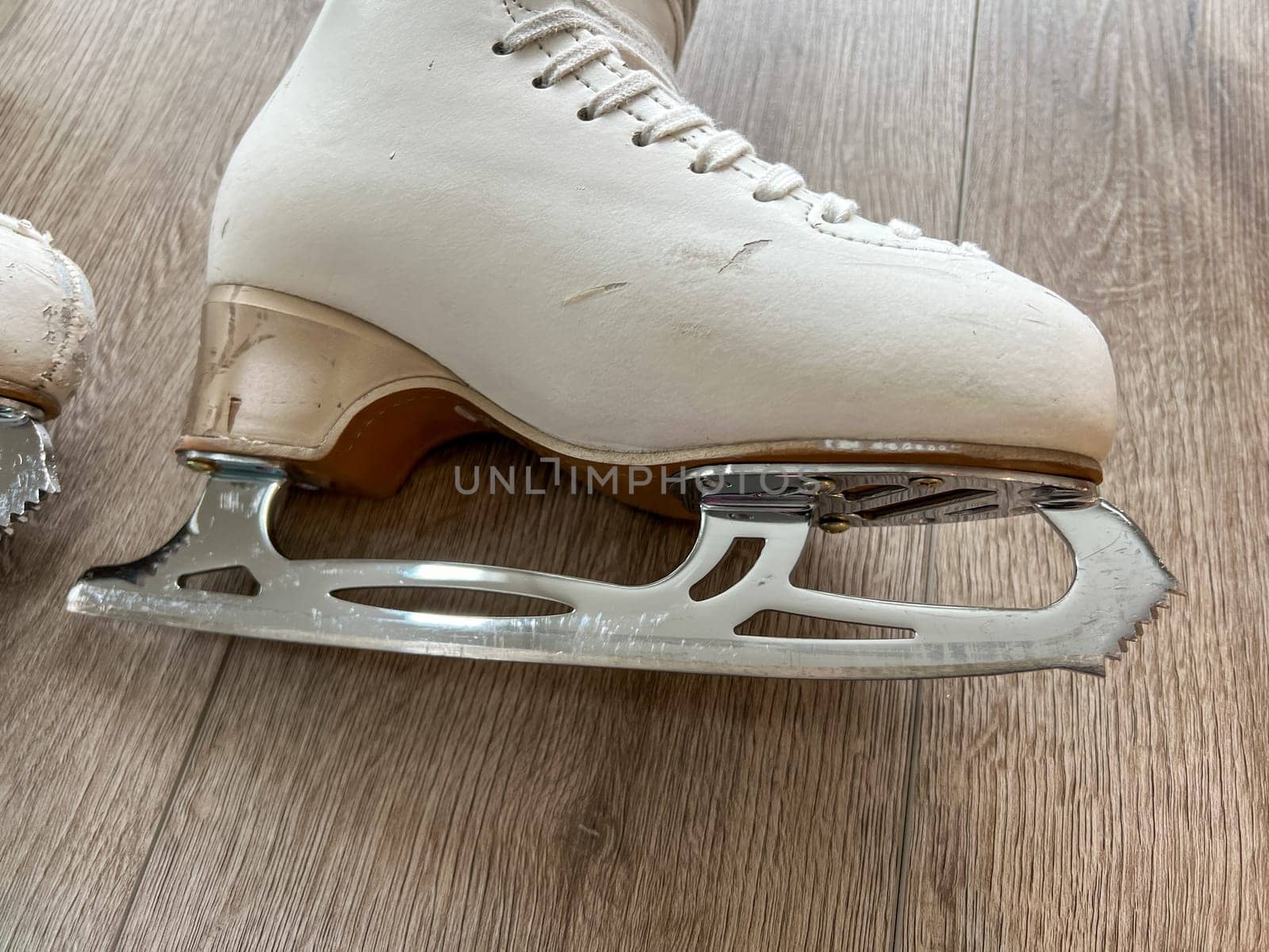 Denver, Colorado, USA-April 20, 2024-A close-up shot of a pair of white ice skates with gold accents, placed on a wooden floor. The skates show signs of use, adding character to the image.