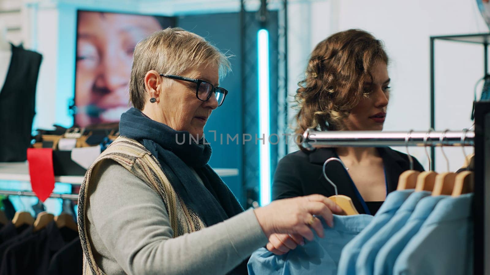 Retail worker suggesting fashion items to elderly customer in clothing store by DCStudio